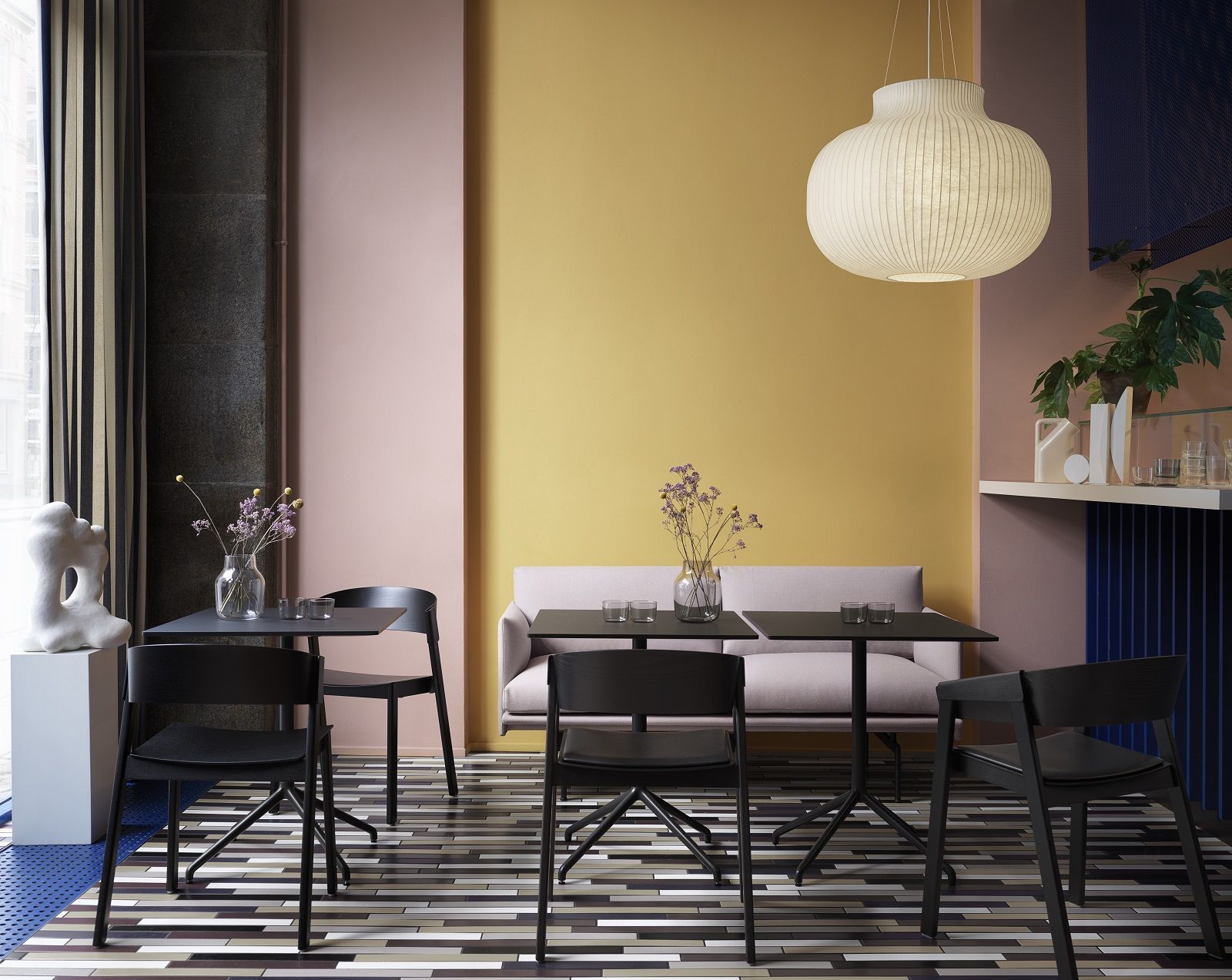 Muuto Outline Studio Sofa 170 cm in hellem Rosa, kombiniert mit schwarzen Tischen und Stühlen.