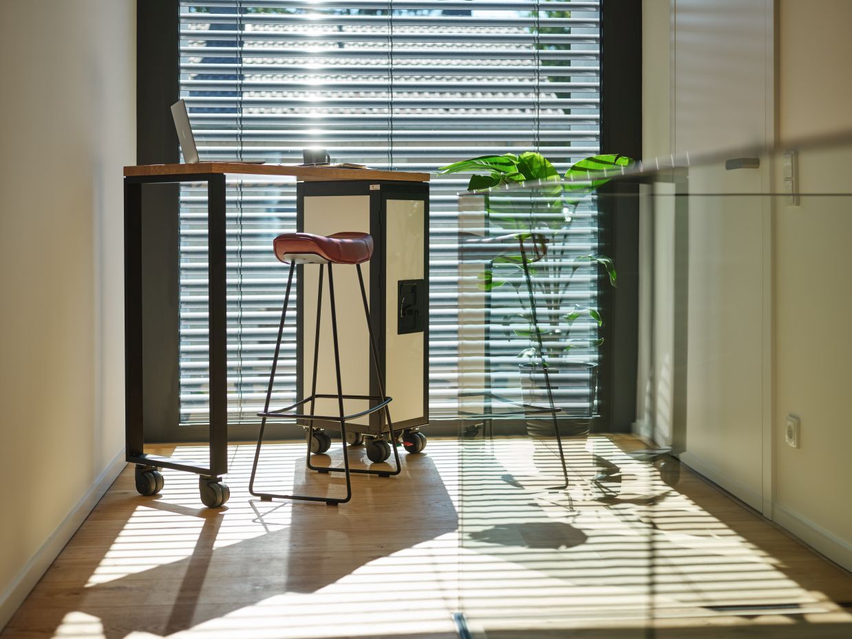 Schwarzer Janua Hightable Tisch mit Bordbar und Barhocker vor einem Fenster mit Jalousien.