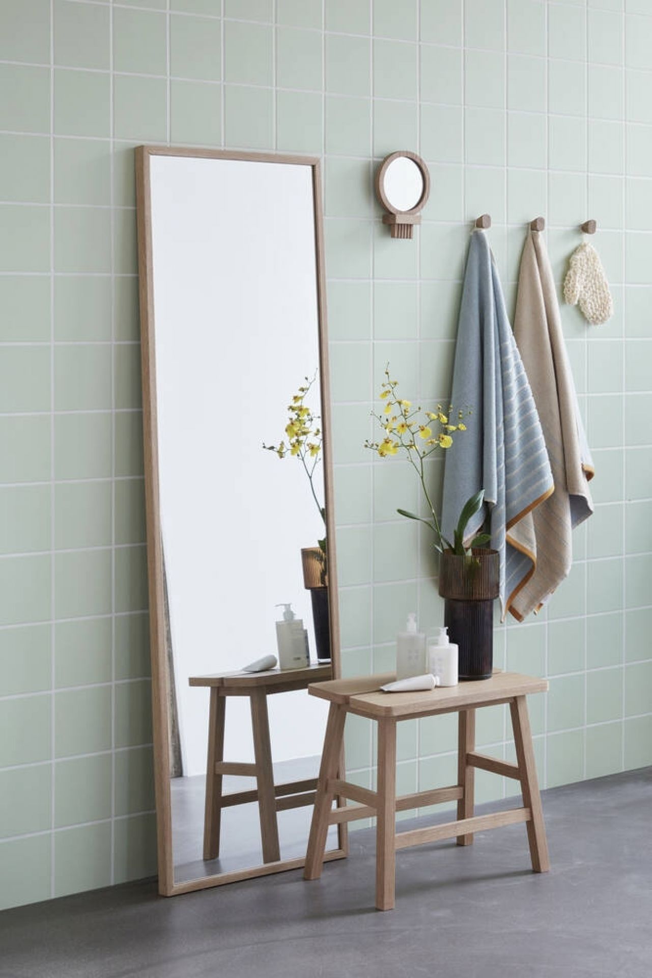 Hübsch Interior Wandspiegel aus Eiche im Badezimmer mit Hocker, Handtüchern und grünen Fliesen.