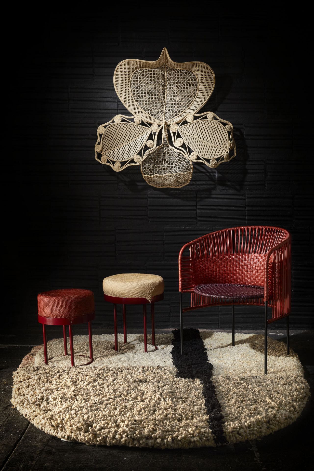 Ames Teppich Nudo large, Wollteppich mit Stühlen und Hockern vor schwarzer Wand.