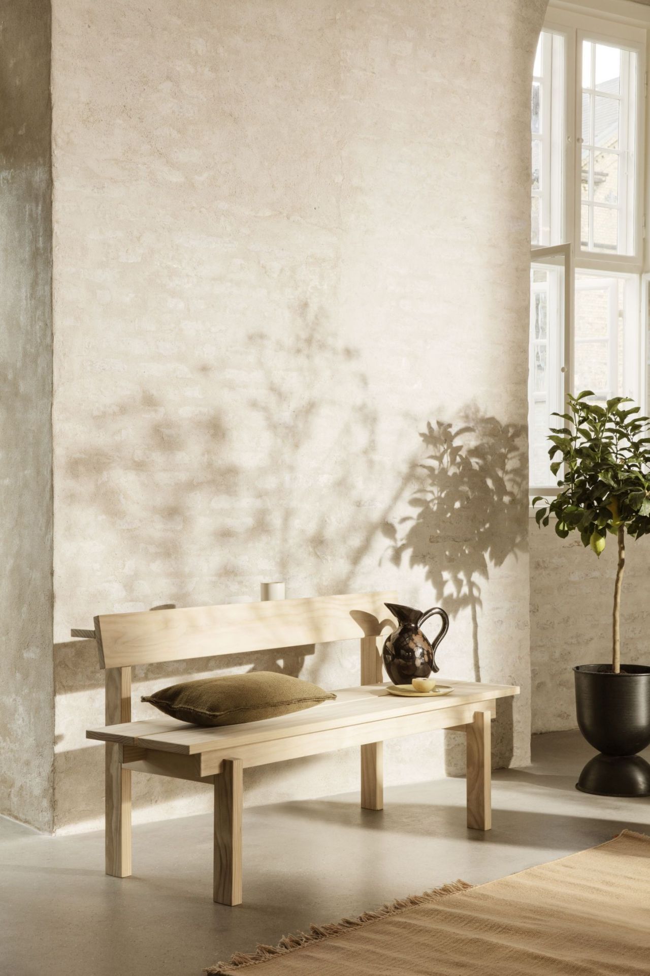 Helle Holzbank, vermutlich Peka Bank, mit Kissen und Dekoration in einem minimalistischen Interieur.