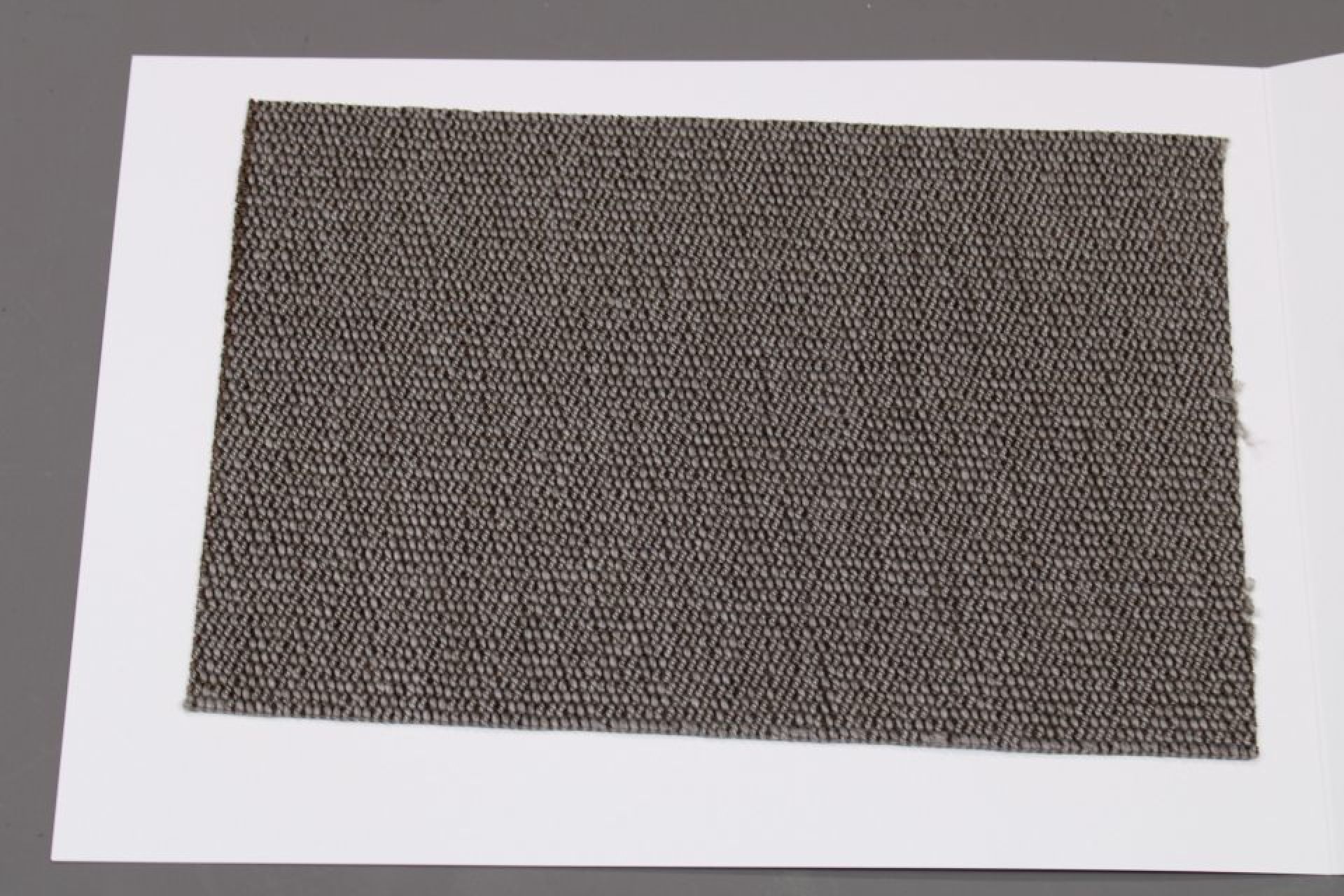 Stoffmusterkarte Gruppe 91 Cor: Nahaufnahme eines grauen, texturierten Möbelstoffes auf weißem Karton.