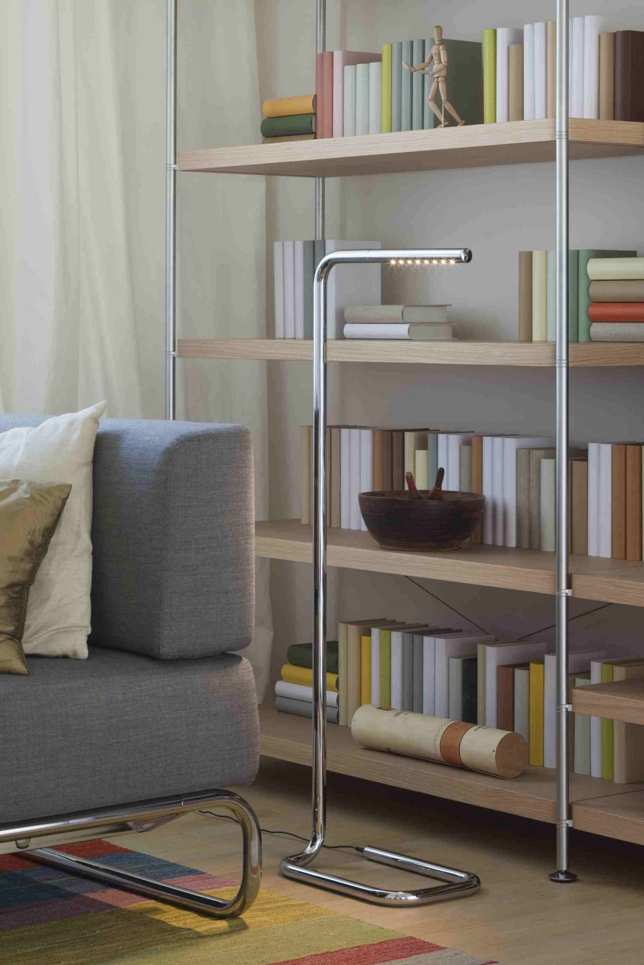 Lum LED Stehleuchte von Thonet, verchromt, im Wohnzimmer neben Regal und Sofa.