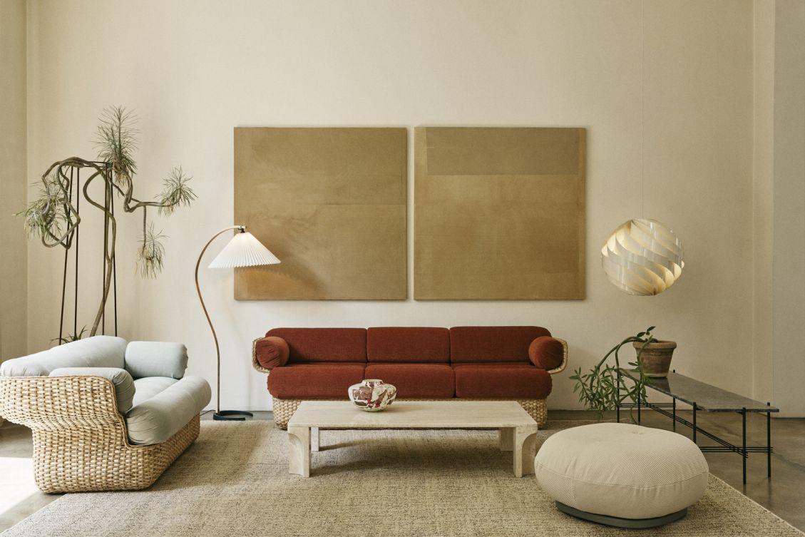 Wohnzimmer Interieur mit Gubi Timberline Stehleuchte, Rattansofa, rotem Sofa, Couchtisch und dekorativer Hängeleuchte.