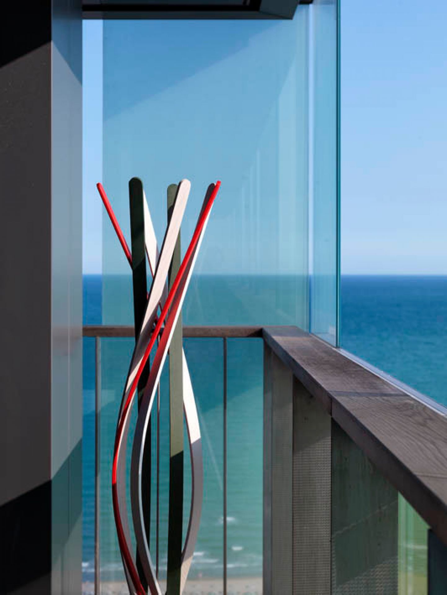 Casamania Horm Twist Garderobenständer aus Buchenholz in Natur auf einem Balkon mit Meerblick.