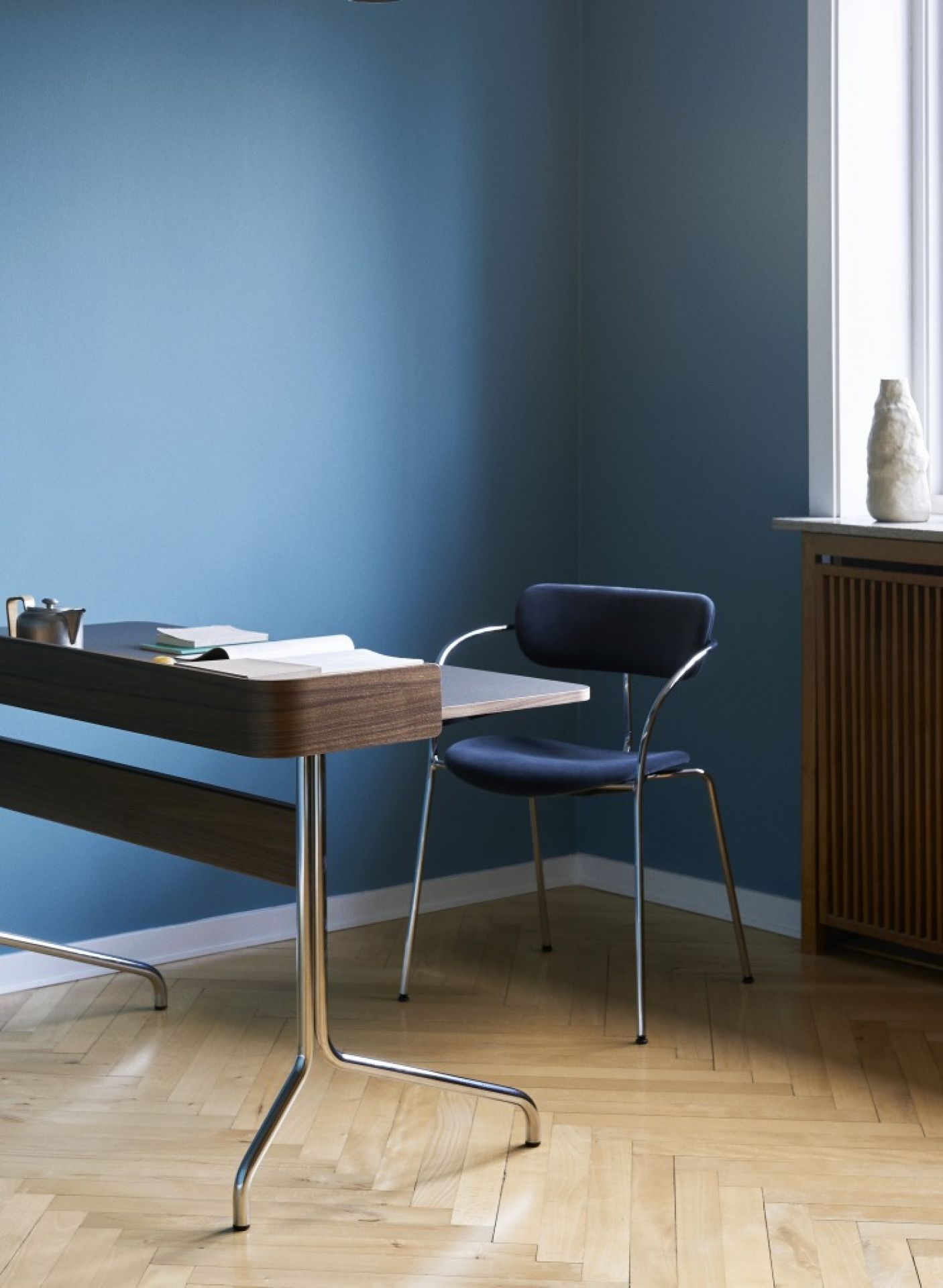 AndTradition Pavilion Schreibtisch AV16/AV17 aus Holz und Chrom, mit Stuhl in einem blauen Raum.