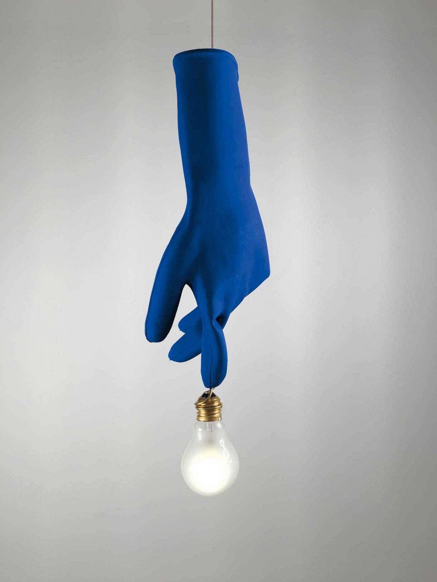 Blaue Luzy Hängeleuchte: Detailaufnahme einer blauen Gummihand, die eine leuchtende Glühbirne hält. Designlampe für Wohnraum.