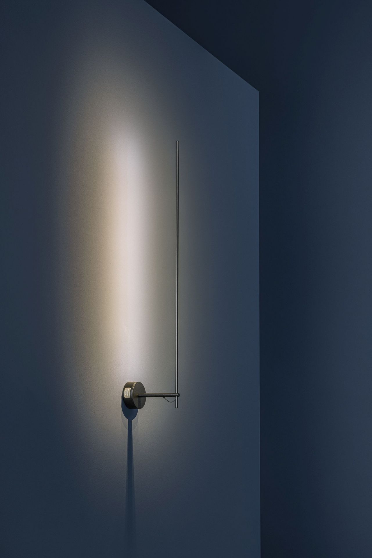 Schwarze Catellani & Smith Light Stick Wandleuchte an blauer Wand, minimalistisches Design, indirekte Beleuchtung.