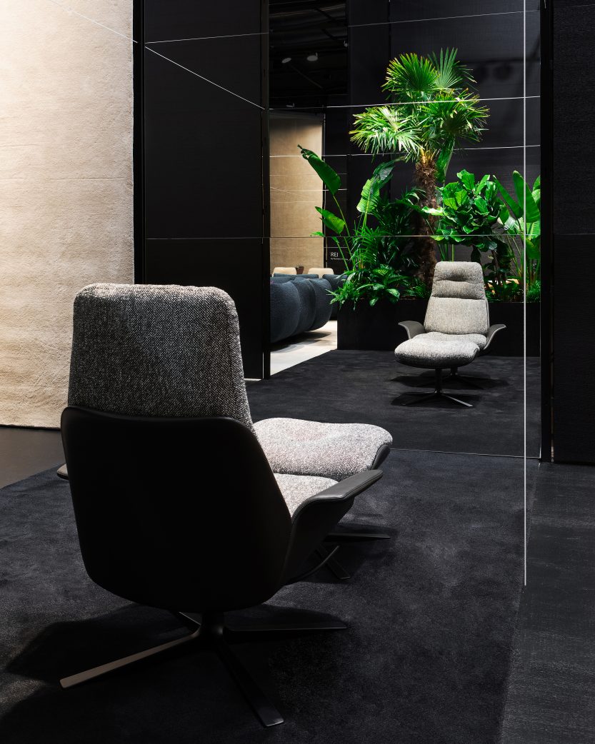 Rei Hocker von Prostoria, grauer Sessel mit schwarzer Rückseite und Drehfuß auf dunklem Teppich.