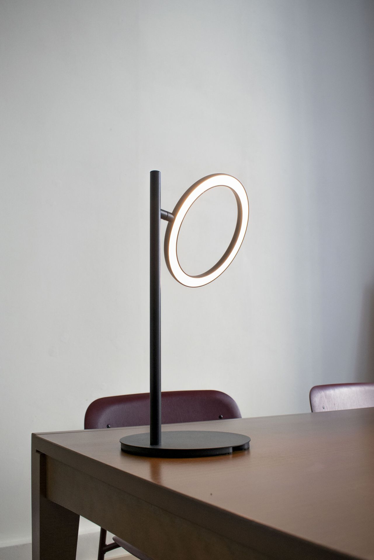 Echo Tischleuchte: Moderne LED-Tischlampe mit ringförmigem Leuchtkörper auf einem Holztisch.