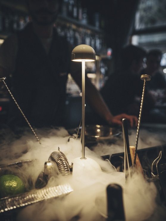 Sips Akkuleuchte in Grün/Gold auf einer Bar mit Cocktail-Zubehör und Trockeneis.