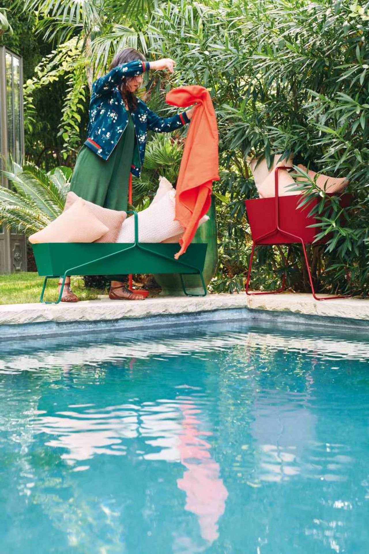 Frau drapiert Tuch über grünen Fermob Basket Blumenkasten am Pool. Roter Blumenkasten im Hintergrund.