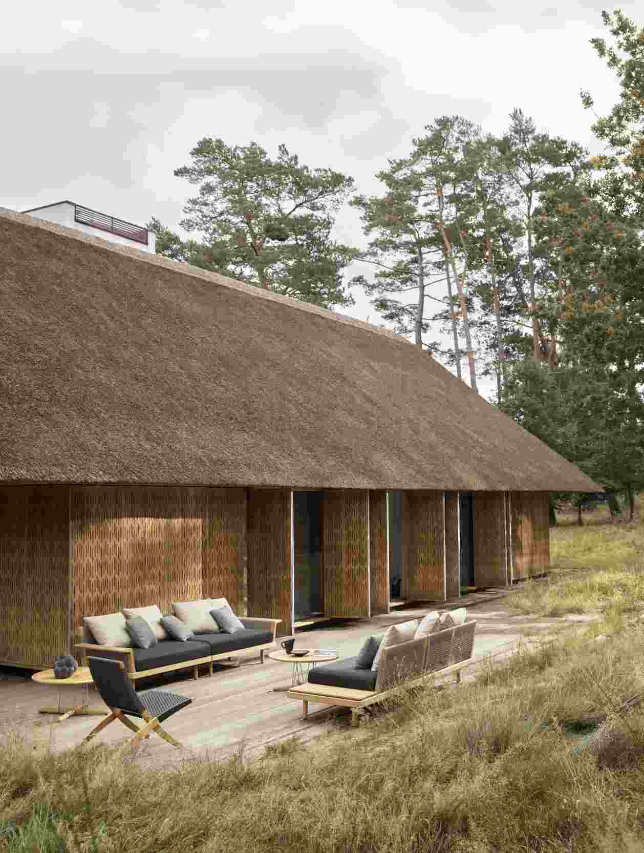 E023 Embrace Lounge Tisch Outdoor von Carl Hansen & Søn vor strohgedecktem Haus.