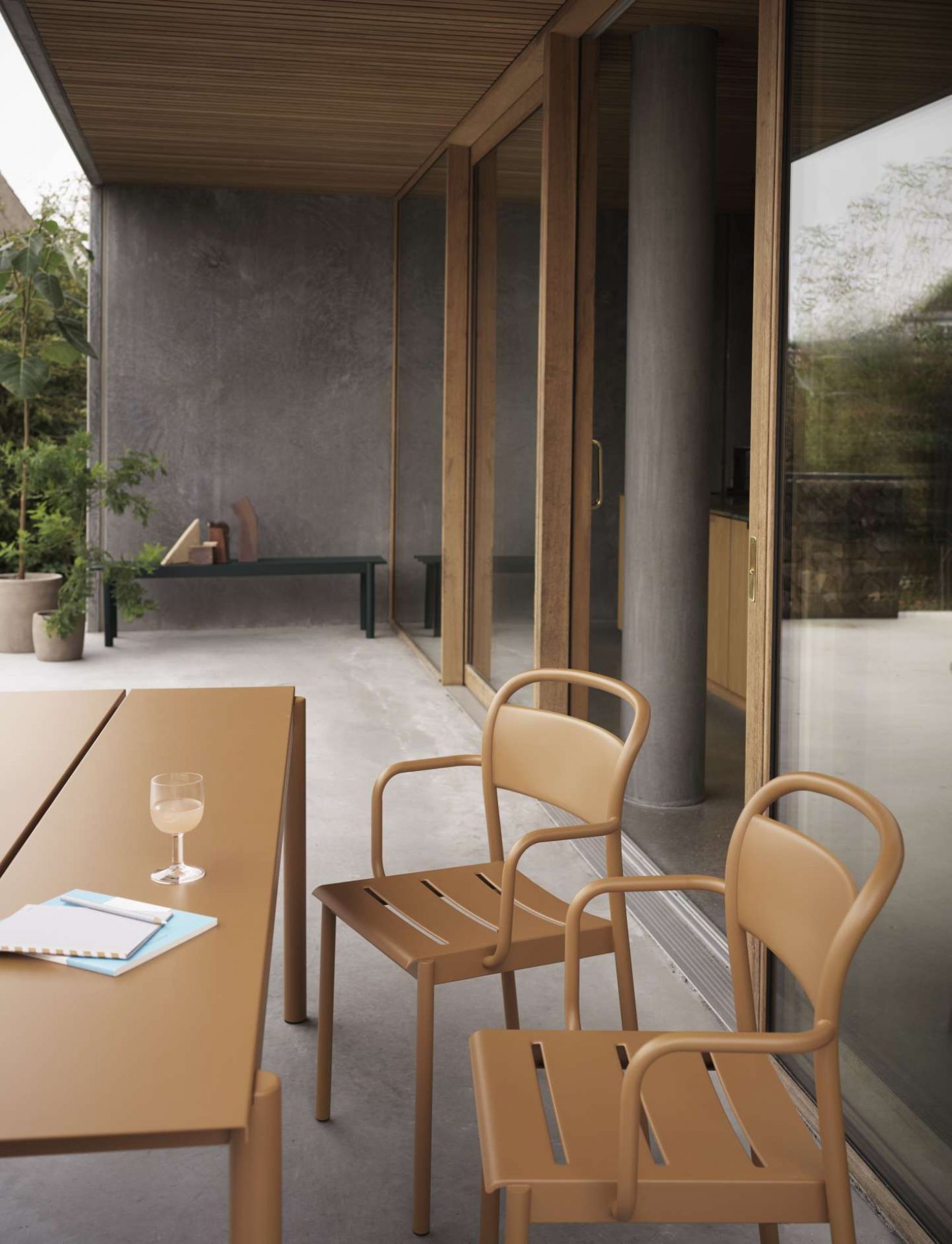 Zwei graue Muuto Linear Steel Armchair Outdoor Armlehnenstühle auf einer Terrasse mit Tisch.