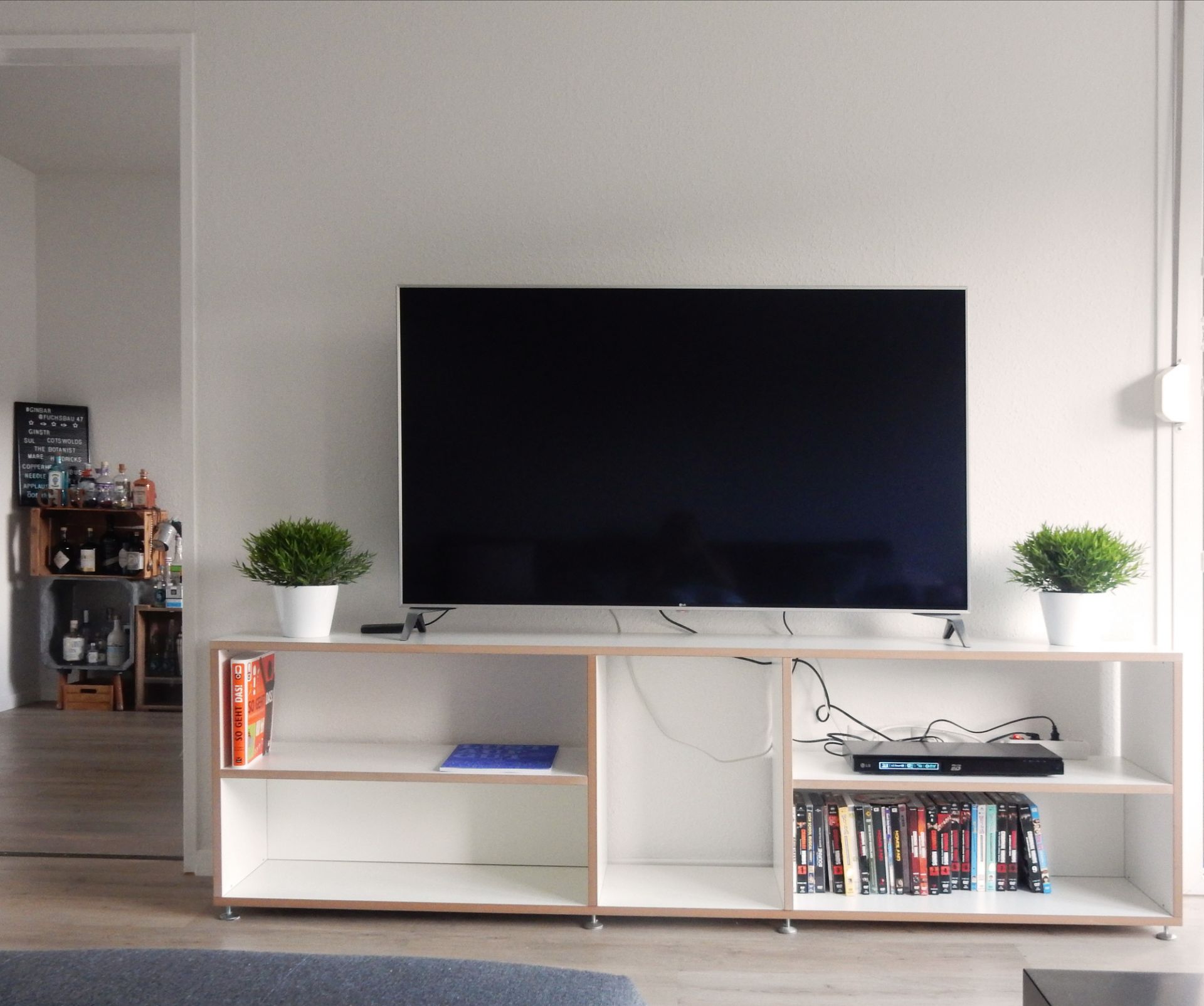 Helles Wohnzimmer mit niedrigem Hanibal Regal von Tojo unter einem Fernseher.