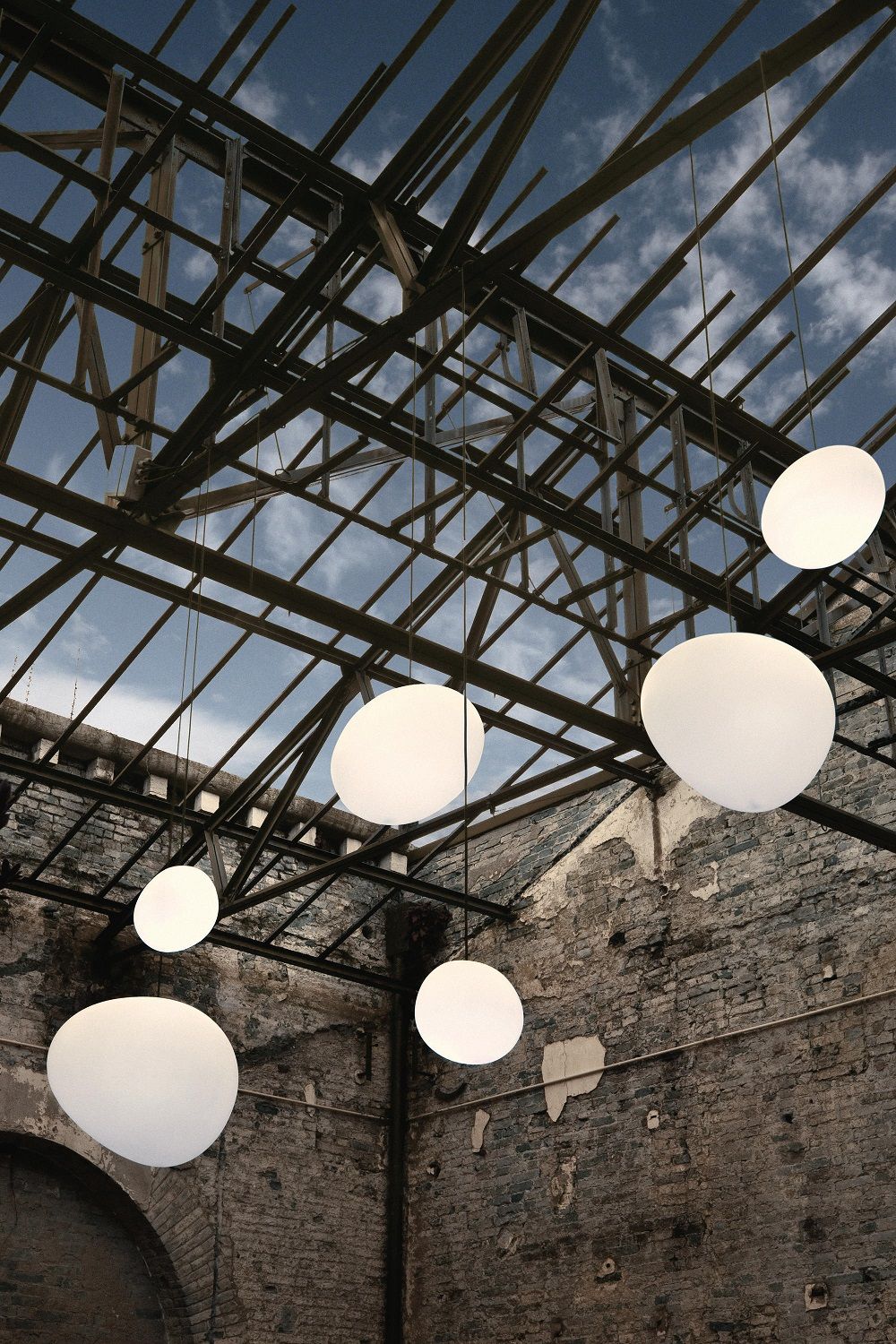 Mehrere weiße Gregg Pendelleuchten von Foscarini hängen unter einem offenen Dach. Outdoor-Beleuchtung.