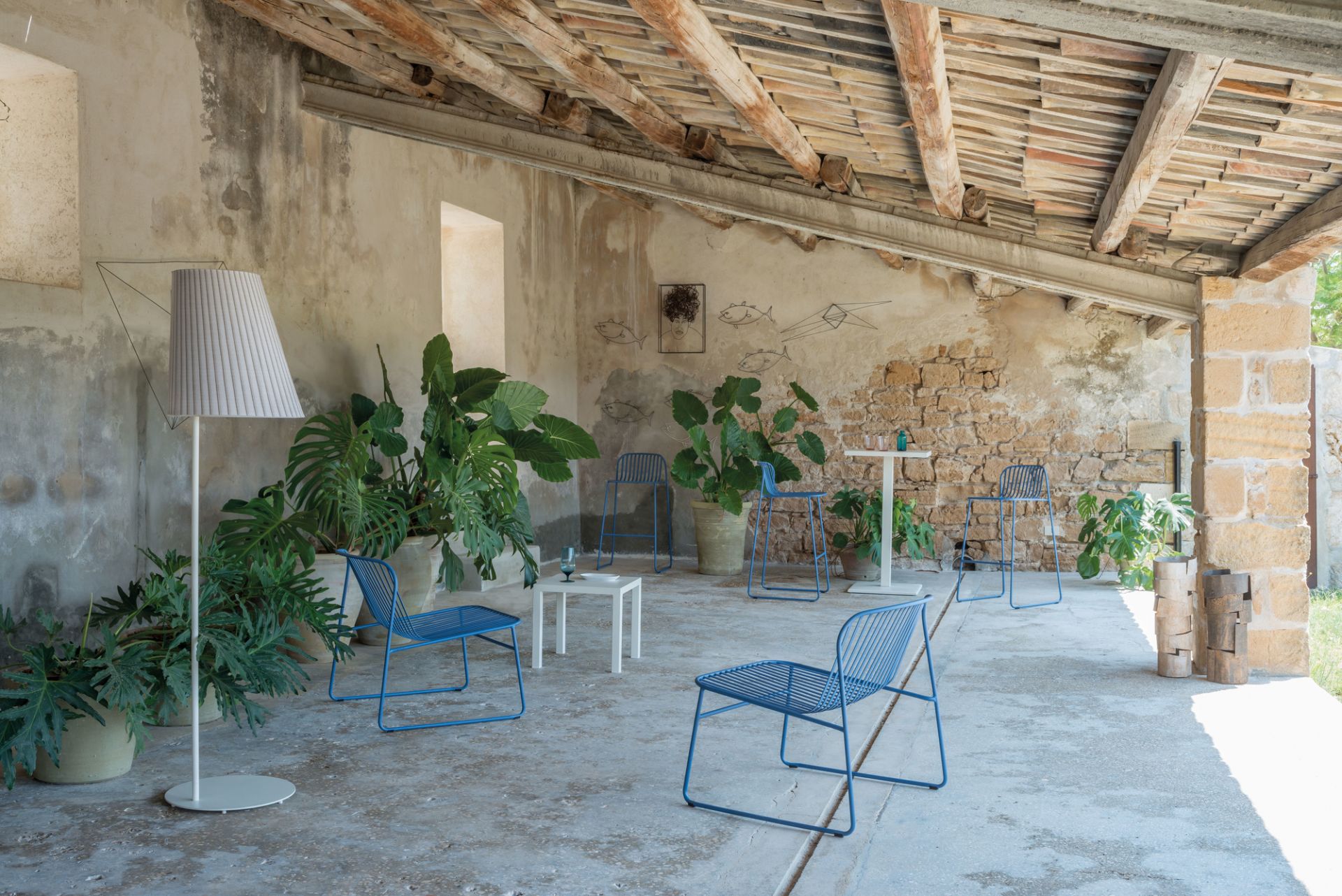 Blauer Riviera Stuhl von Emu im Aussenbereich, umgeben von Pflanzen und rustikalem Mauerwerk.