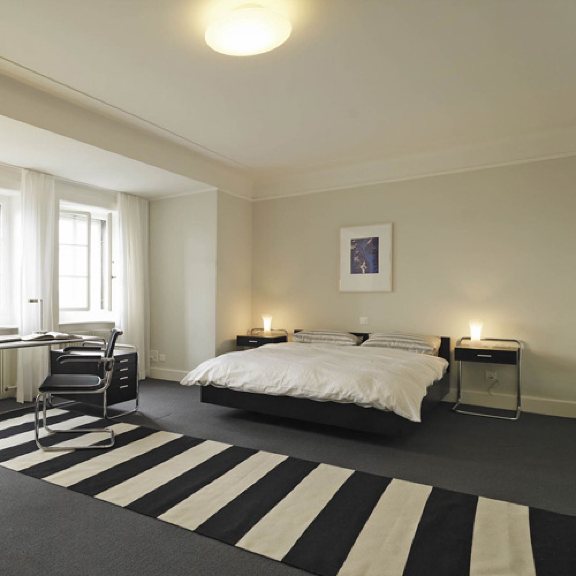 Schlafzimmer mit Thonet B 117 Beistelltischen mit Schublade neben einem Bett und Schreibtisch.