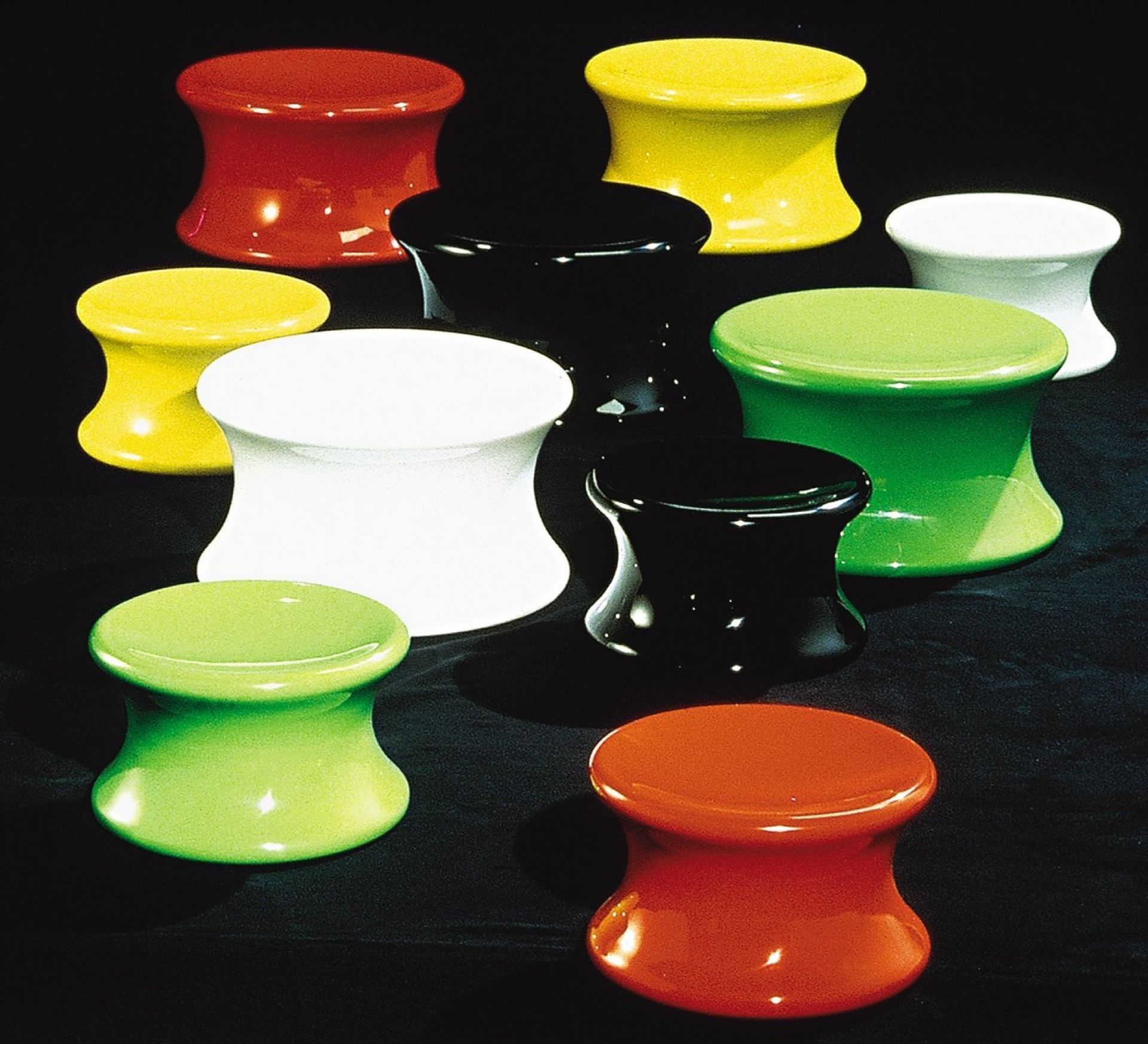 Verschiedenfarbige Mushroom Hocker, darunter ein kleiner schwarzer Eero Aarnio Hocker, auf schwarzem Hintergrund.