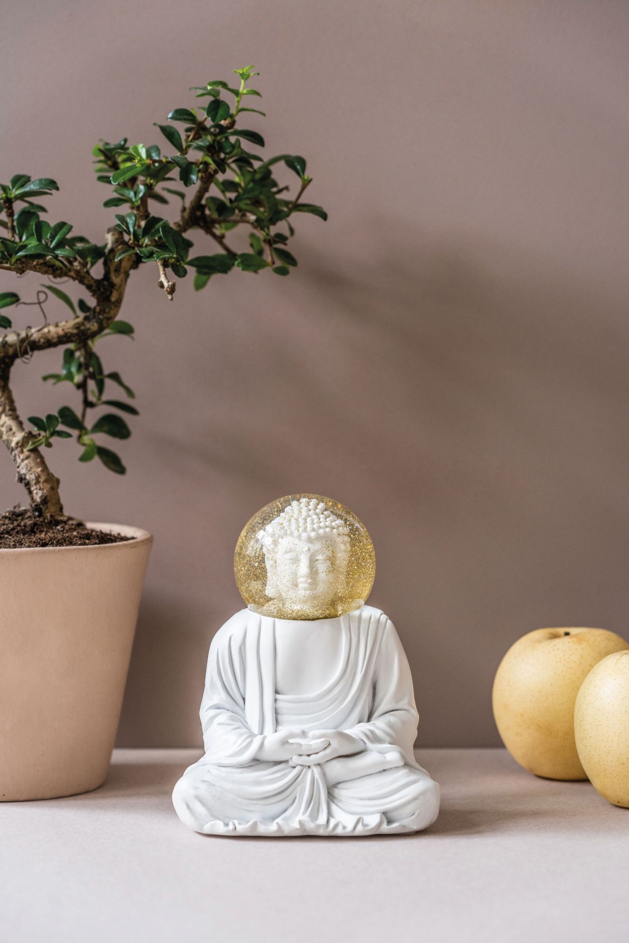 Summerglobes Buddha Glitzerkugel: Weiße Buddha Figur mit goldener Glitzerkugel, Dekoration mit Bonsai und Birnen.