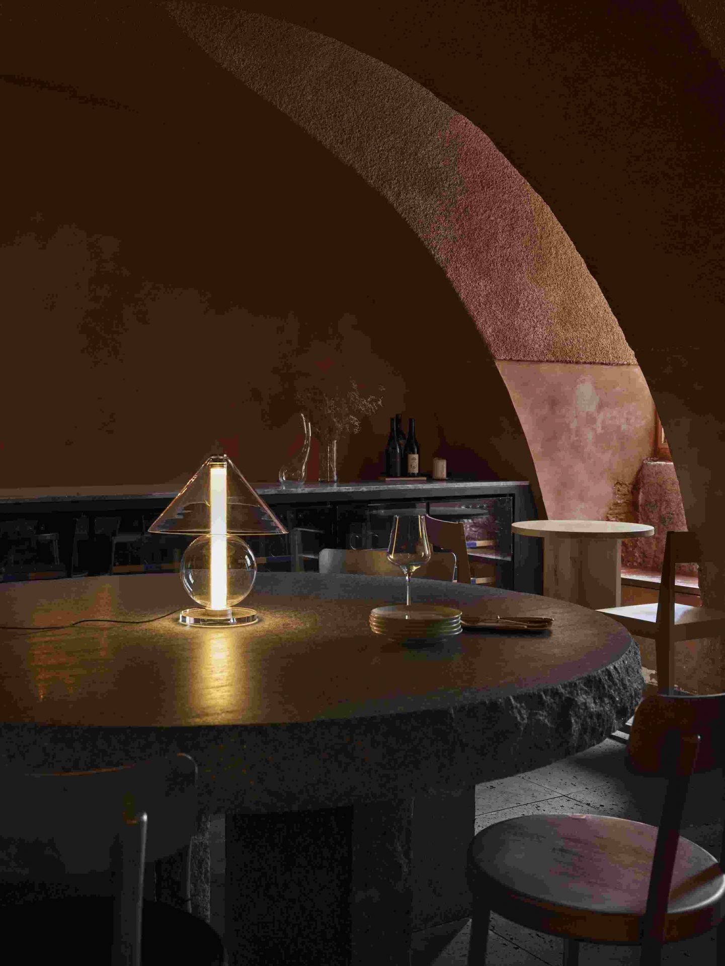 Fragile Tischleuchte von Marset in Bernstein auf einem Steintisch, warmes Licht.