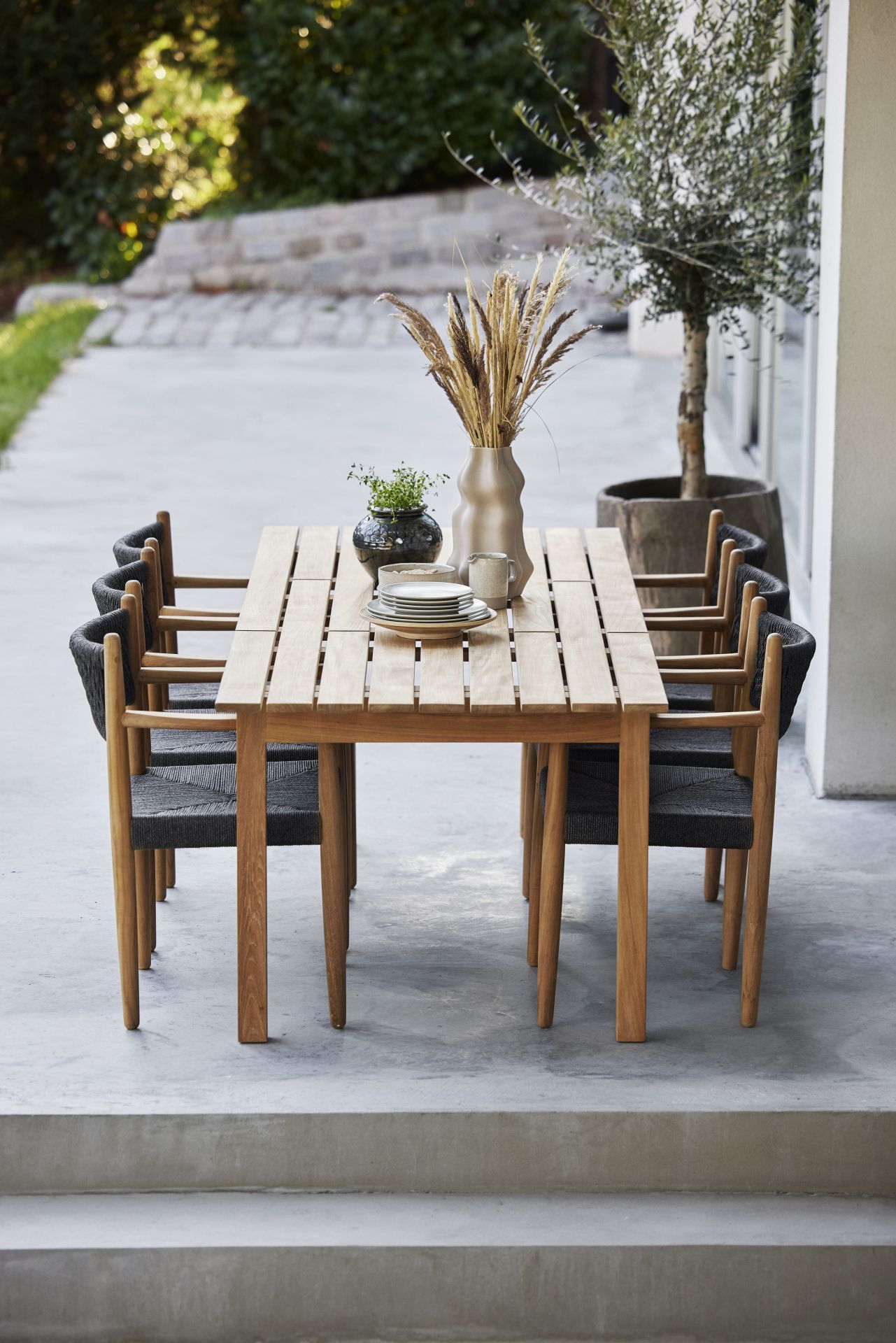 Grace Esstisch von Cane-Line aus Teakholz mit sechs Stühlen und Tischdeko im Außenbereich.