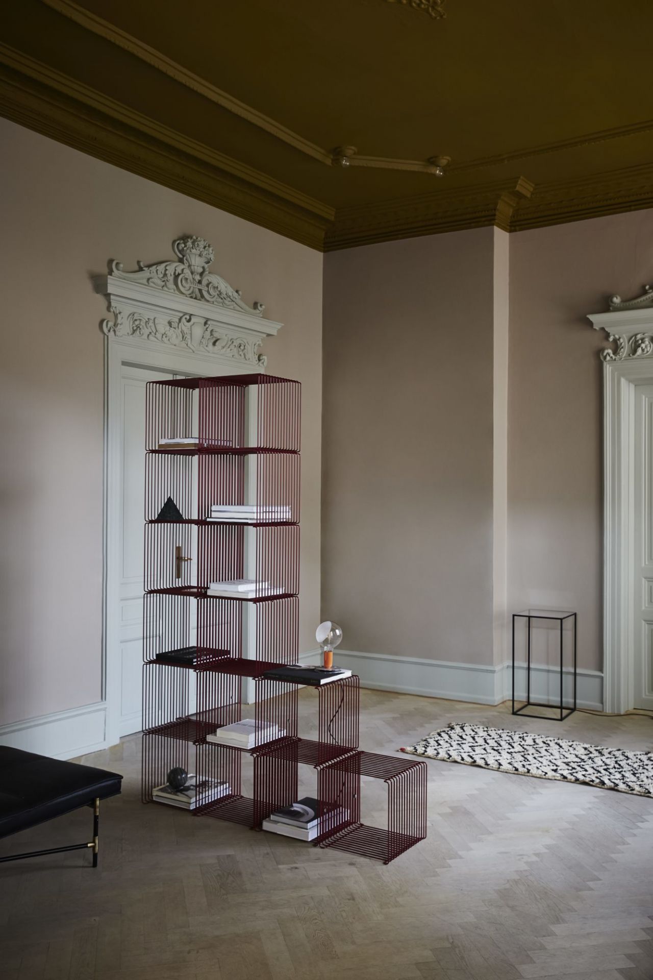 Freistehendes, burgunderrotes Montana Wire Cube Drahtregal im Wohnzimmer, gefüllt mit Büchern und Dekoration, modernes modulares Regalsystem.