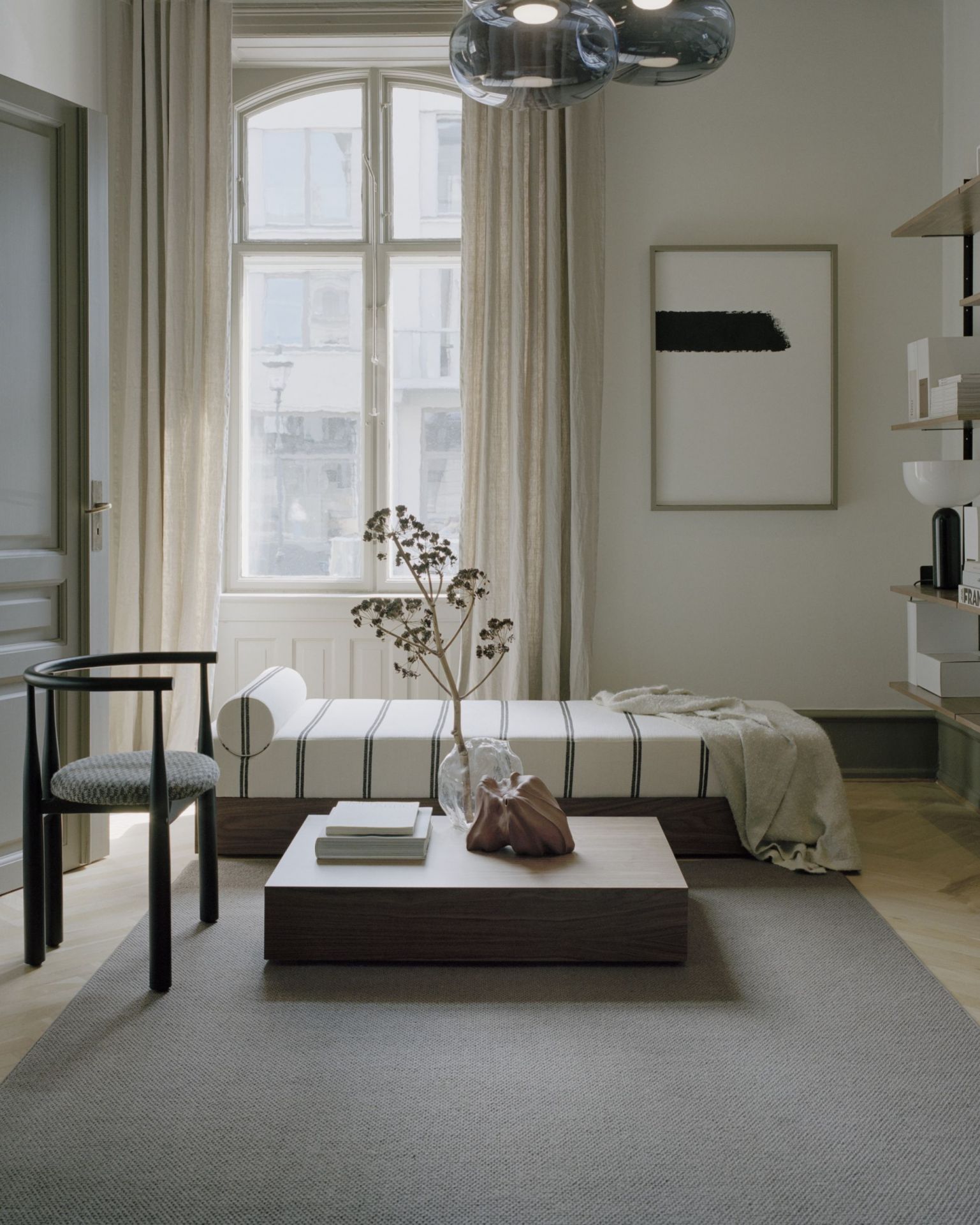 Helles Interieur mit Mass Tagesbett Ohio, schwarzem Holzstuhl und modernem Couchtisch.