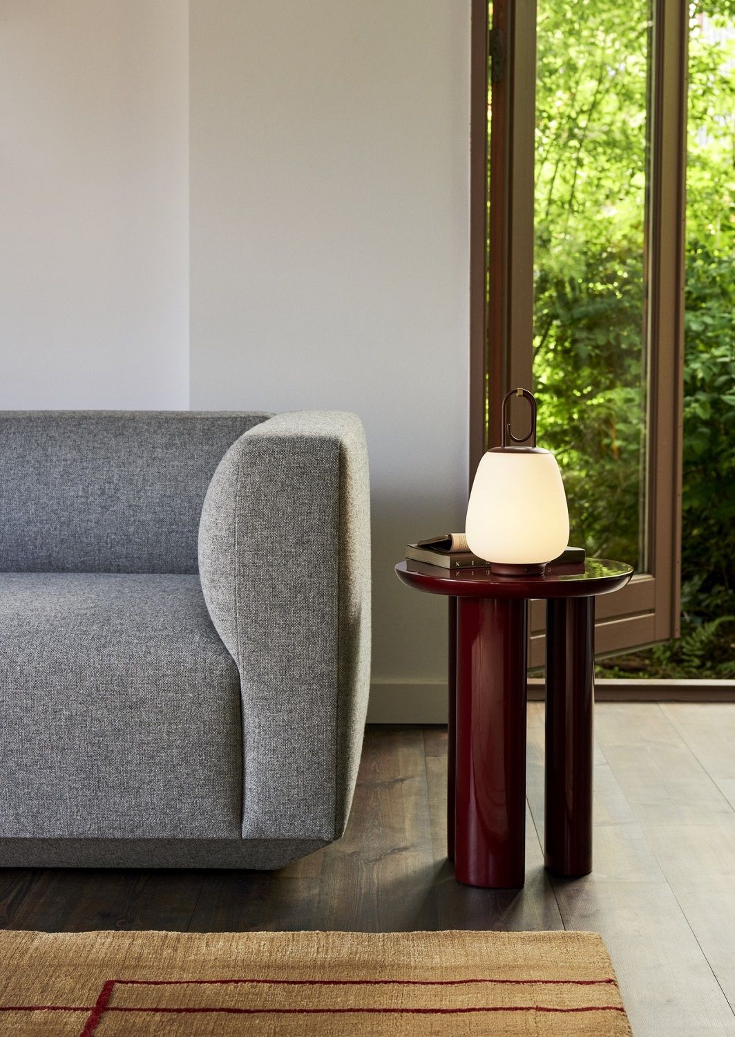 Detailaufnahme: Graues Develius Sofa von AndTradition neben rotem Beistelltisch und Lampe. Modernes Wohnzimmer-Interieur.