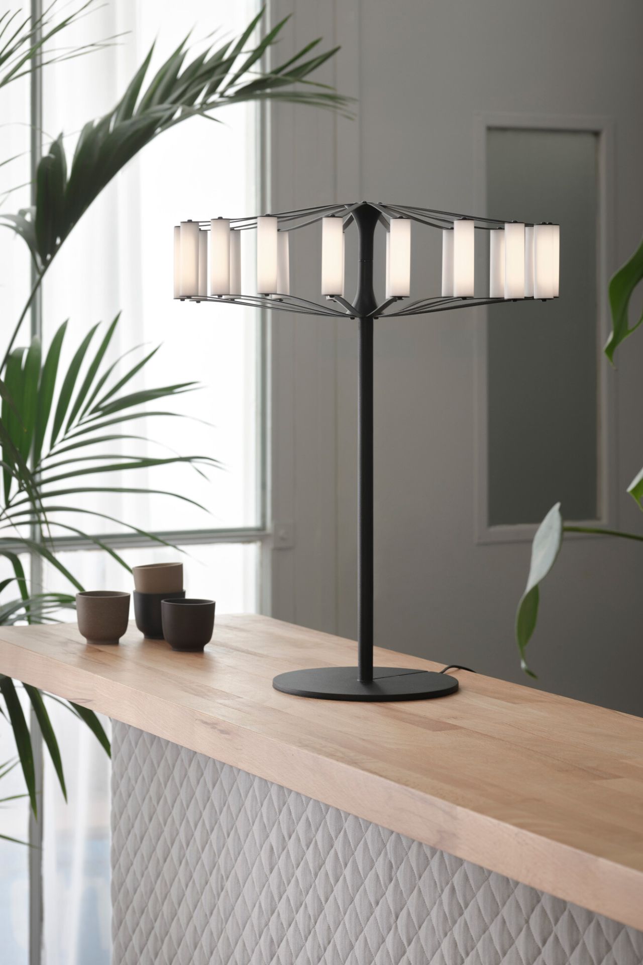 Wheel Table Tischleuchte Japth, moderne Lampe mit schwarzem Gestell und zylindrischen Leuchtelementen auf einem Holztisch.