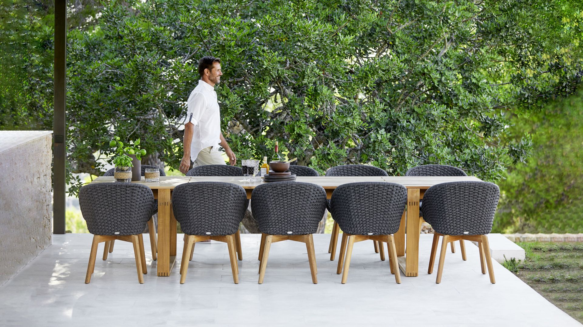 Endless Esstisch von Cane-Line aus Teakholz mit grauen Flechtstühlen für den Außenbereich.
