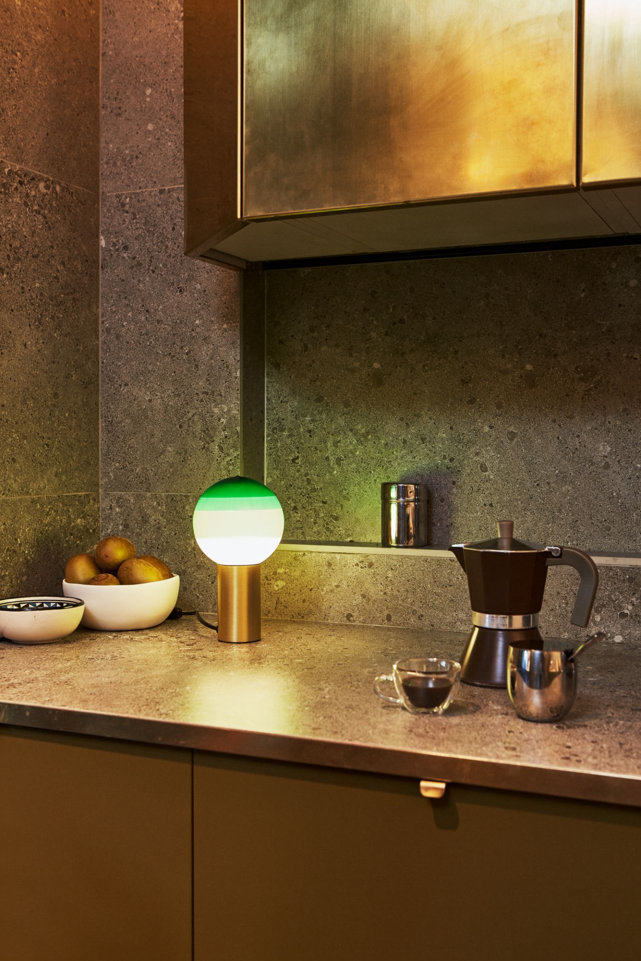 Dipping Light S LED Tischleuchte von Marset auf Küchentheke mit Kaffeekanne und Obstschale.