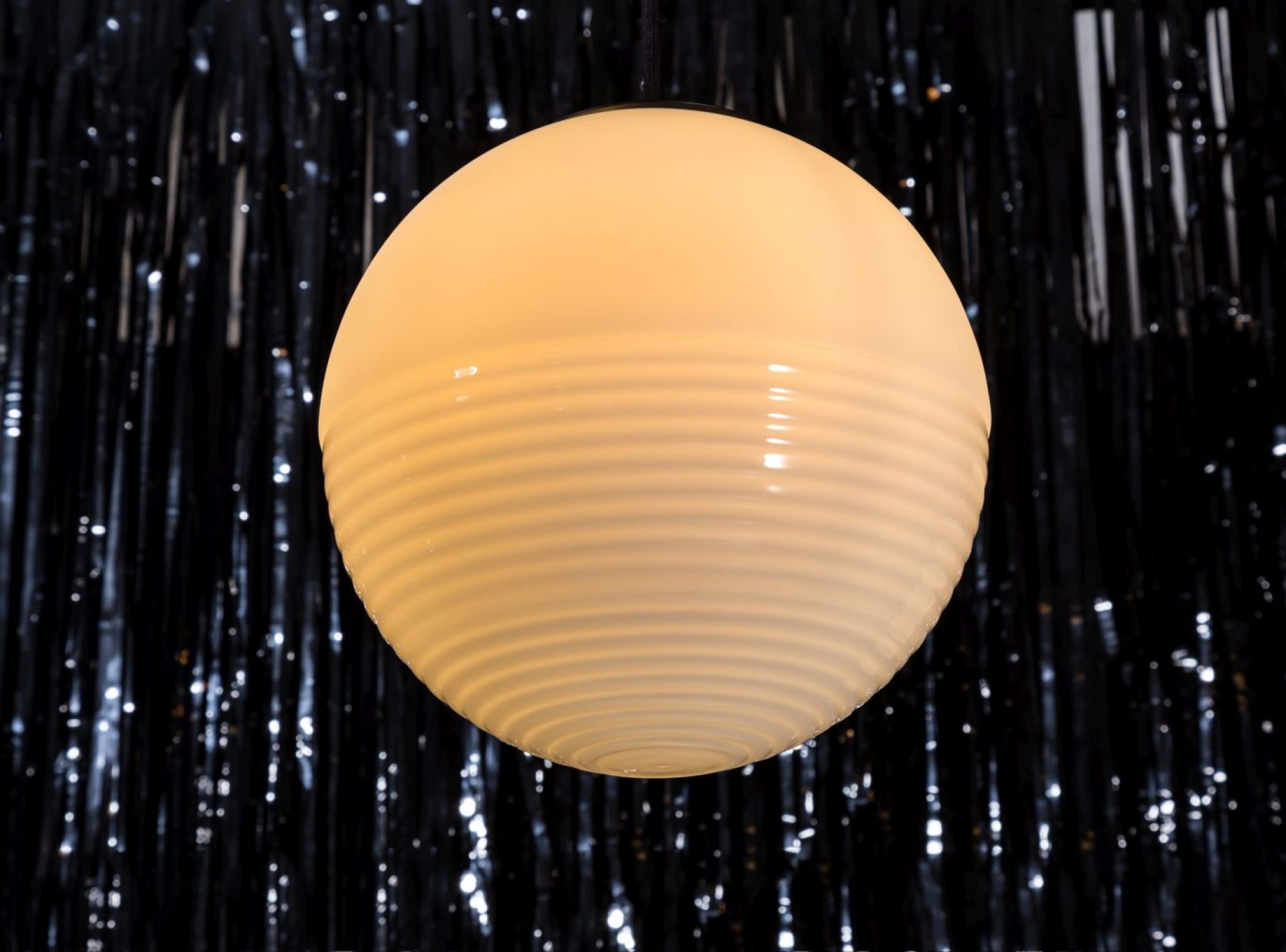 Weiße Stellar Pendelleuchte von Pulpo mit geriffelter Oberfläche vor dunklem Hintergrund. Design Lampe.