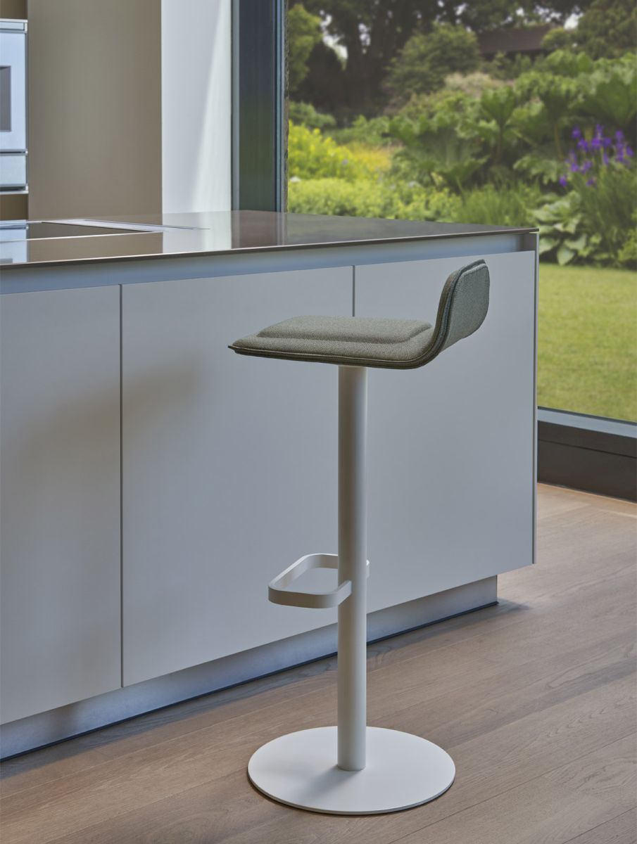 Weißer Dave Barhocker mit salbeifarbenem Sitzpolster vor Kücheninsel und Fenster mit Gartenblick.