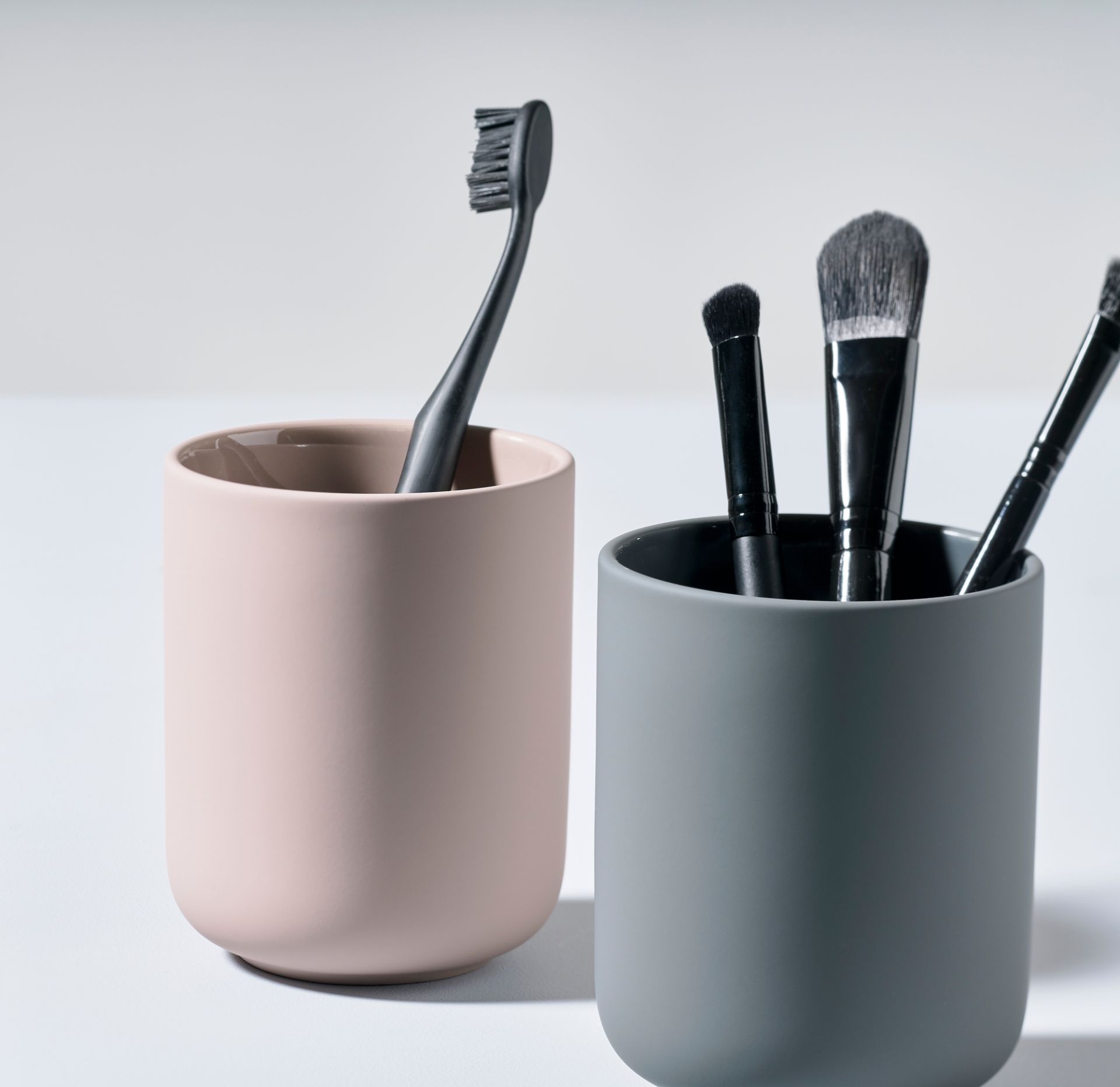 Ume Zahnputzbecher von Zone Denmark in Rosa mit Zahnbürste und grauer Becher mit Make-up-Pinsel.