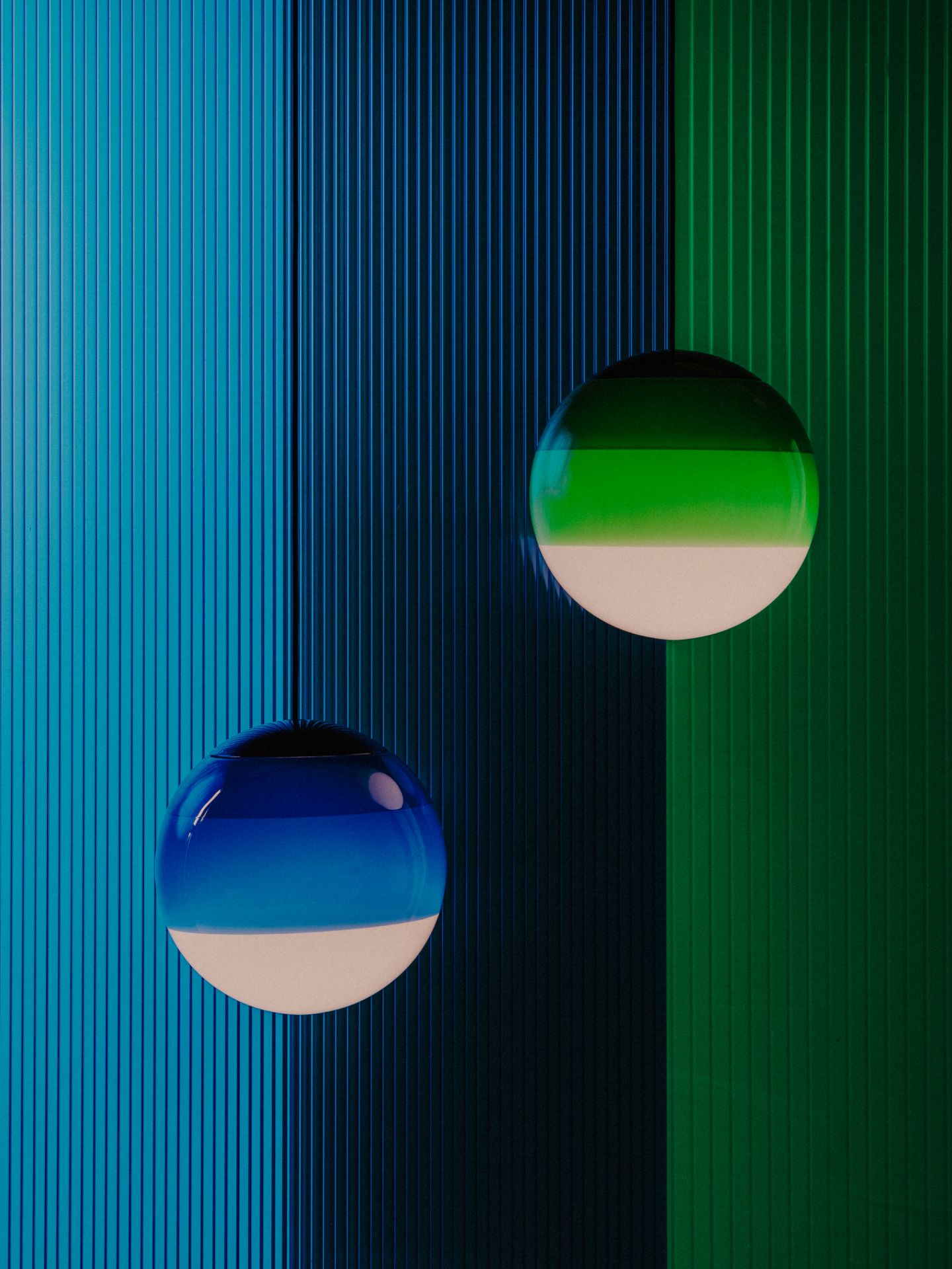 Dipping Light Pendelleuchten in Grün und Blau vor farbigen, geriffelten Hintergründen.