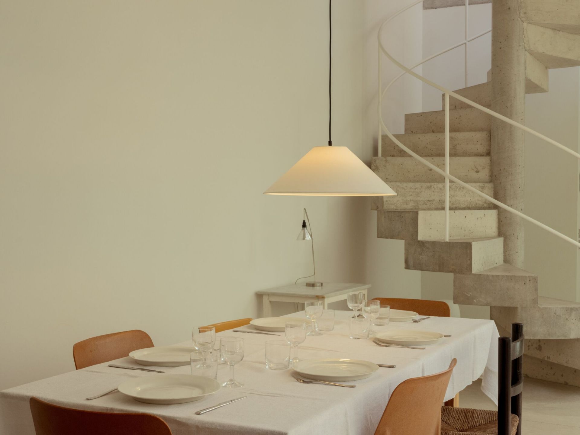 Weiße Sísísí Pendelleuchte von Santa & Cole über Esstisch mit Geschirr und Wendeltreppe im Hintergrund.