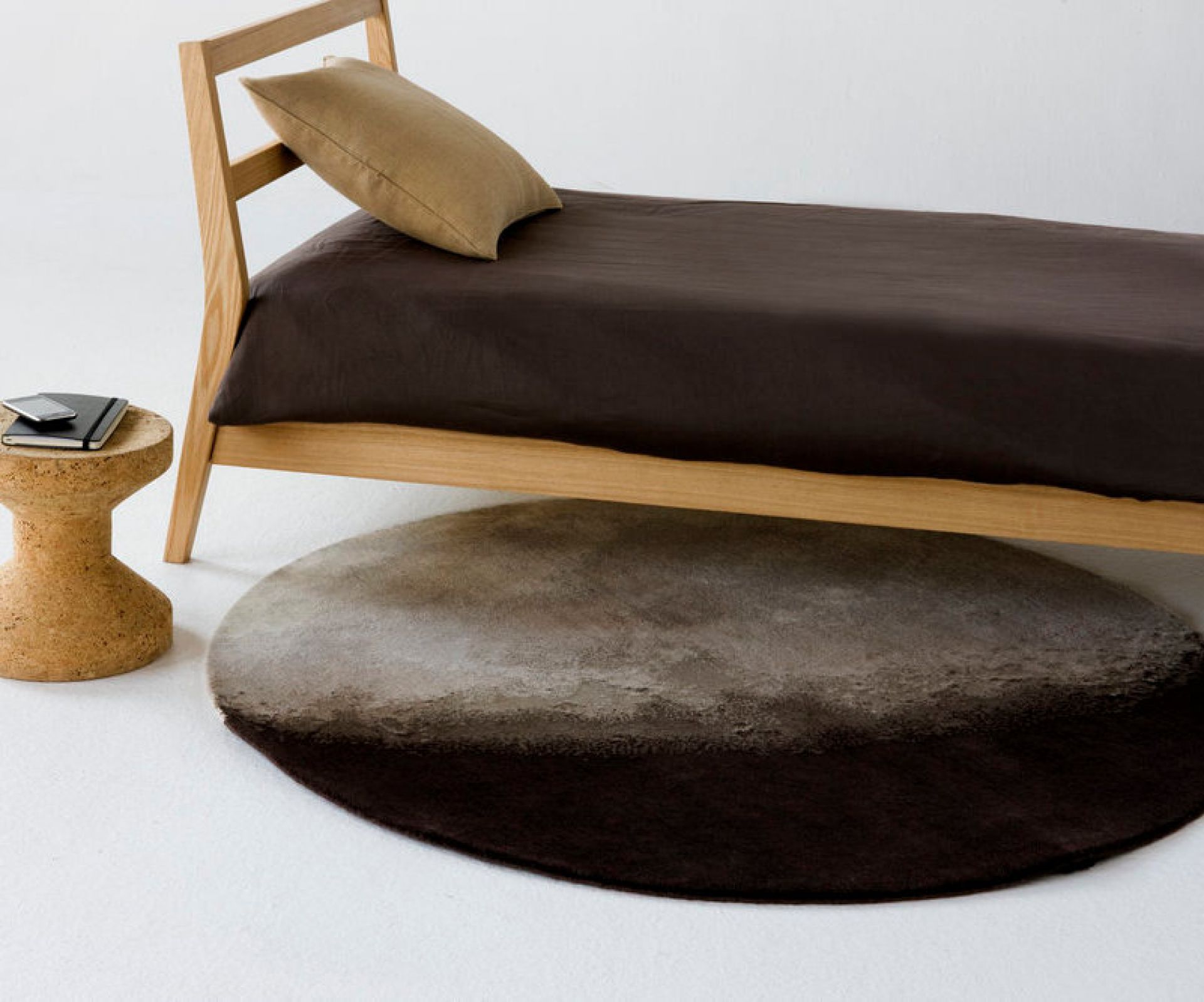 Luna Teppich von Nanimarquina unter einem Bett, runder Wollteppich in Braun- und Grautönen.