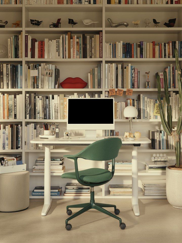 Vitra Tyde 2 Home Desk Steh-Sitz-Schreibtisch in Weiß mit grünem Bürostuhl vor Bücherregal.