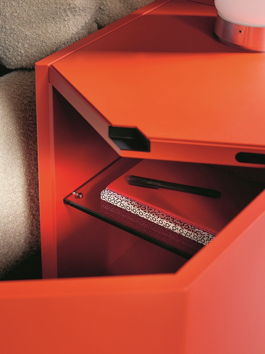 Detailaufnahme des orangefarbenen Z24 Nachttischs von Zanotta mit Glasablage, Notizbuch und Stift.