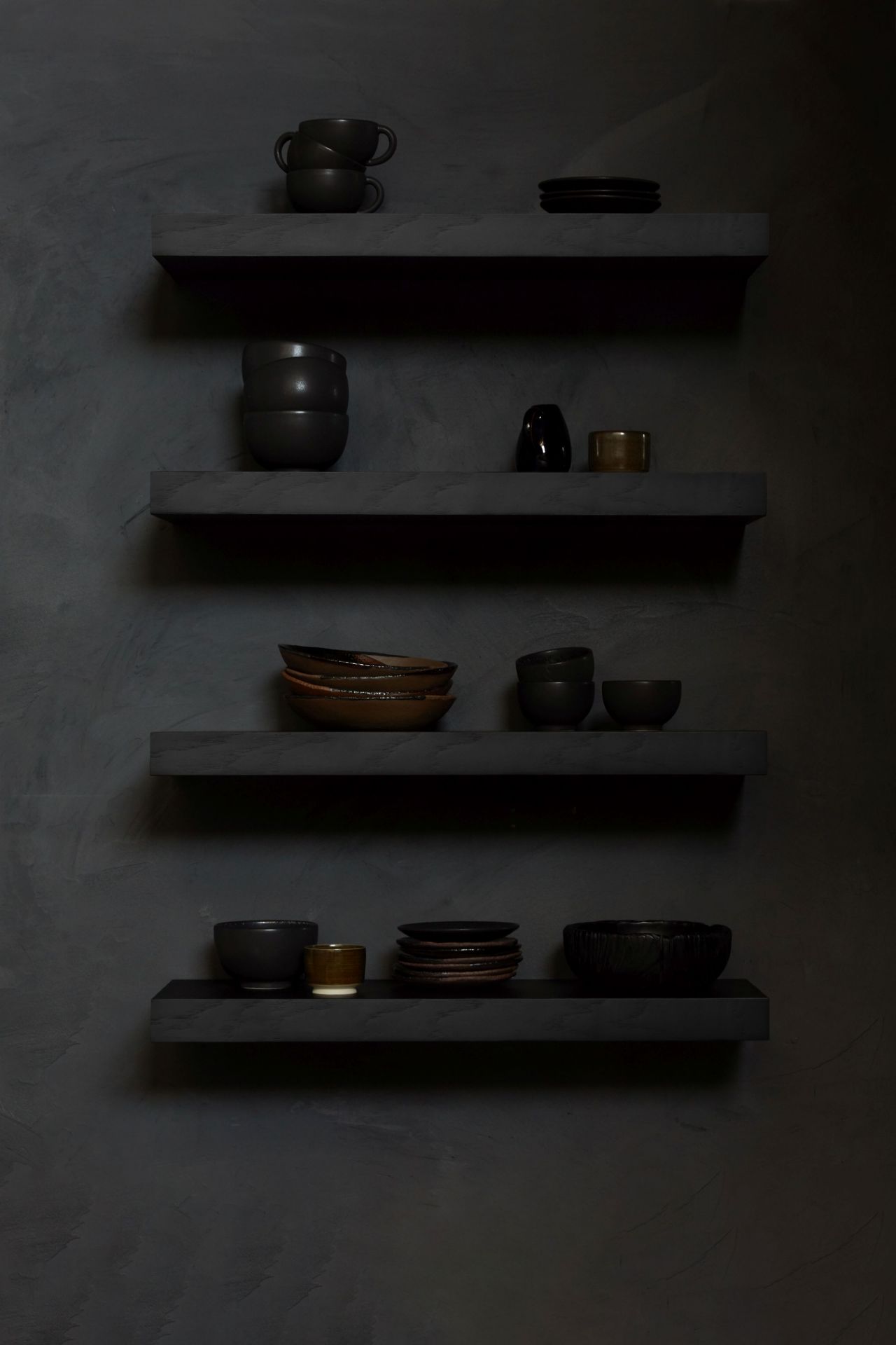 Schwarzes Ethnicraft Wandregal aus Eiche mit lackierter Oberfläche, dekoriert mit Geschirr und Vasen vor dunkler Wand.