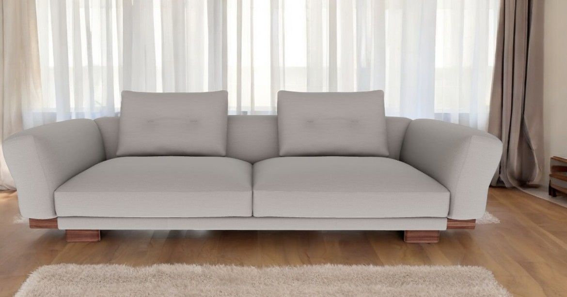 Helles Sengu Sofa mit zwei Kissen und Holzfüßen vor einem Fenster mit Vorhängen.