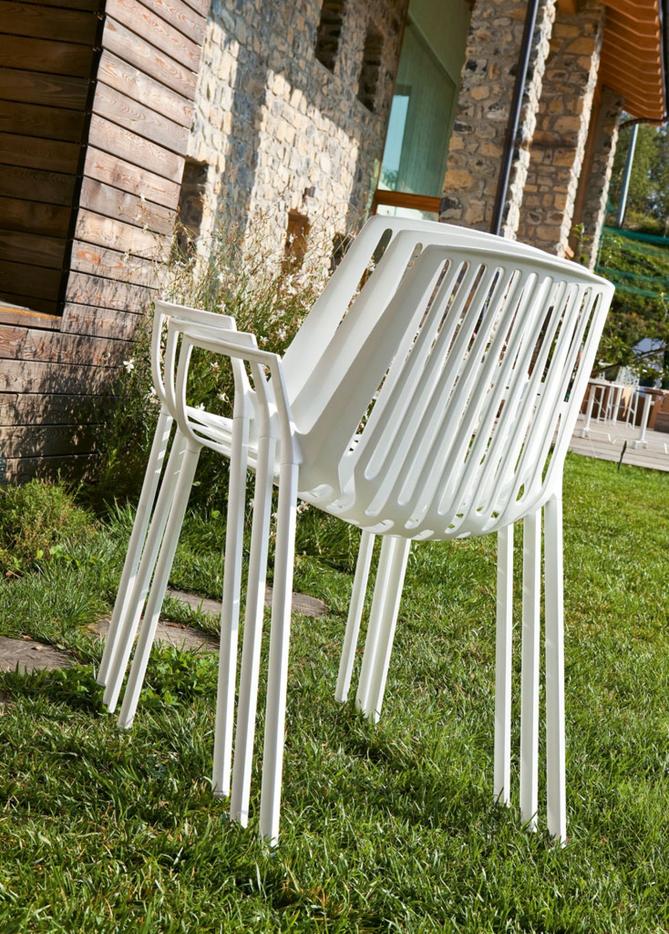 Weißer Rion Outdoor Sessel, gestapelt auf Rasen. Gartenmöbel, Design Sessel für Terrasse und Balkon.