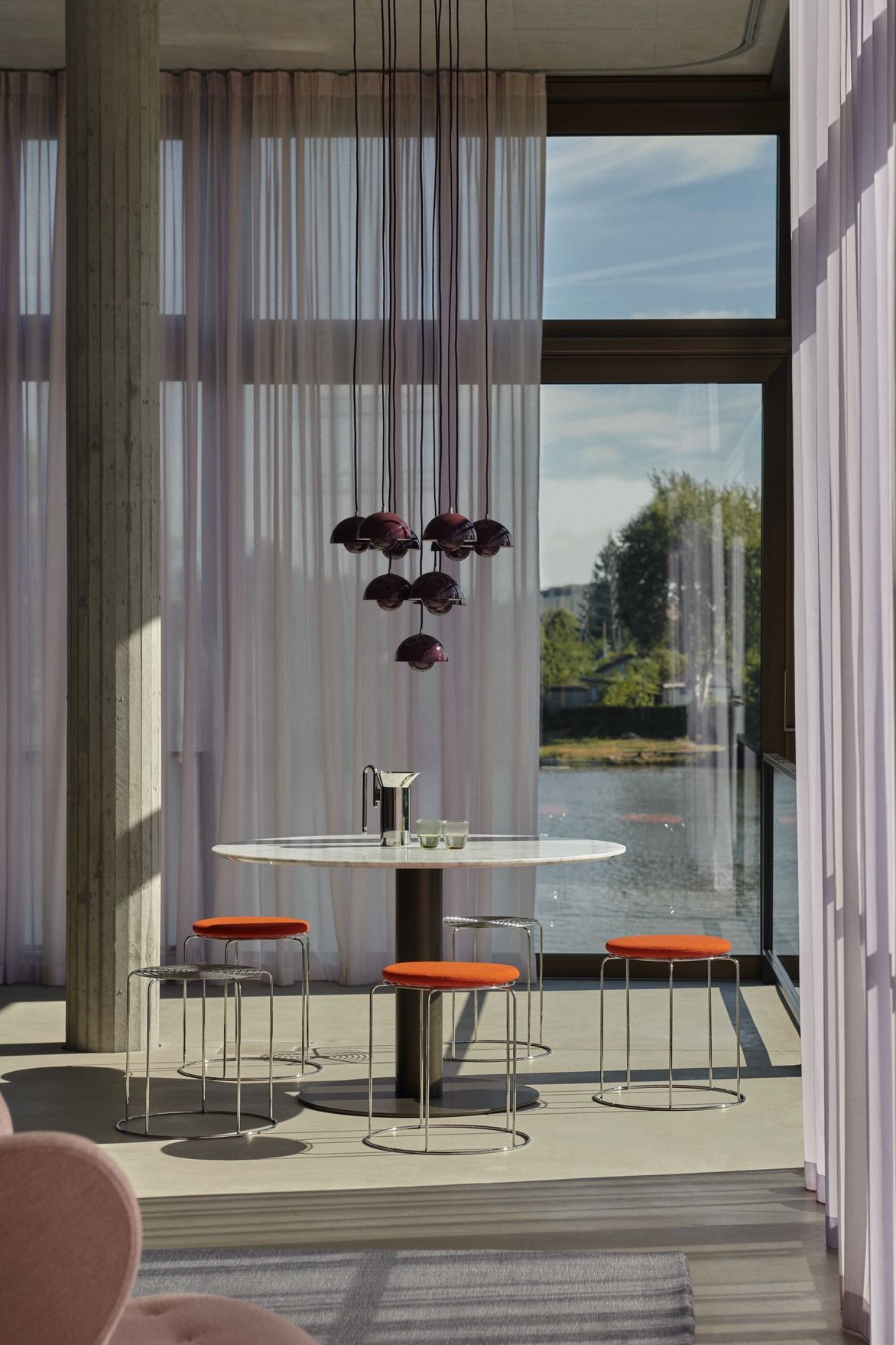 Nahaufnahme von AndTradition Wire Stool VP11 Hockern mit orangefarbenen Seat Pad Sitzkissen an einem Esstisch.