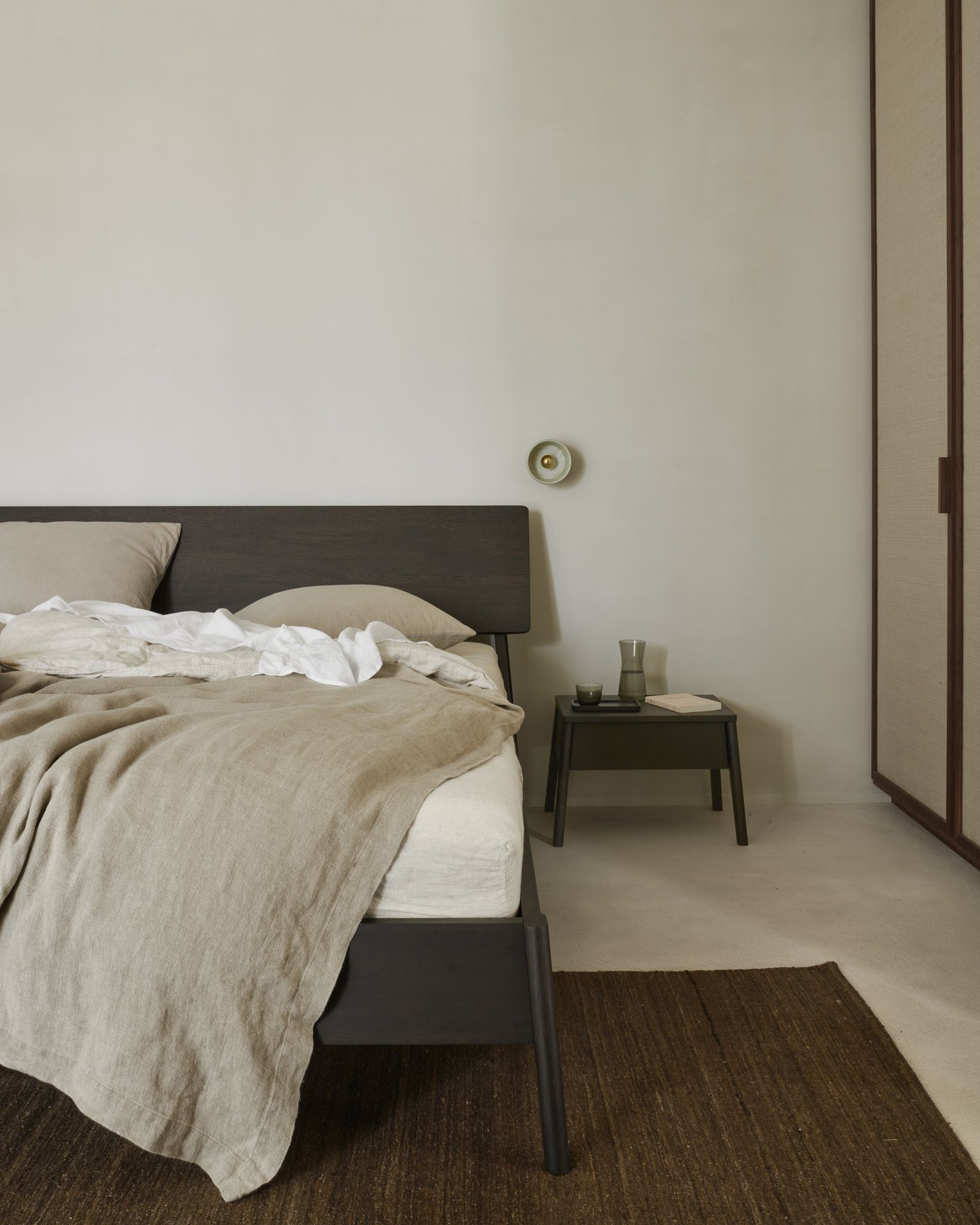 Ethnicraft Air Bett Eiche braun mit Nachttisch und braunem Teppich im Schlafzimmer.