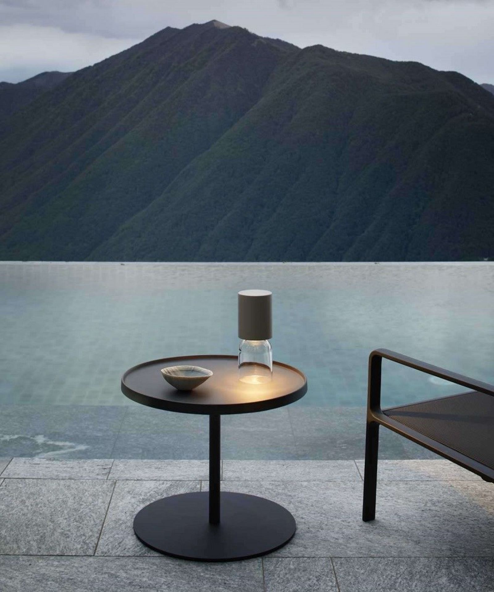 A02R1 NUI Akkuleuchte von Luceplan auf Tisch im Außenbereich mit Bergpanorama.