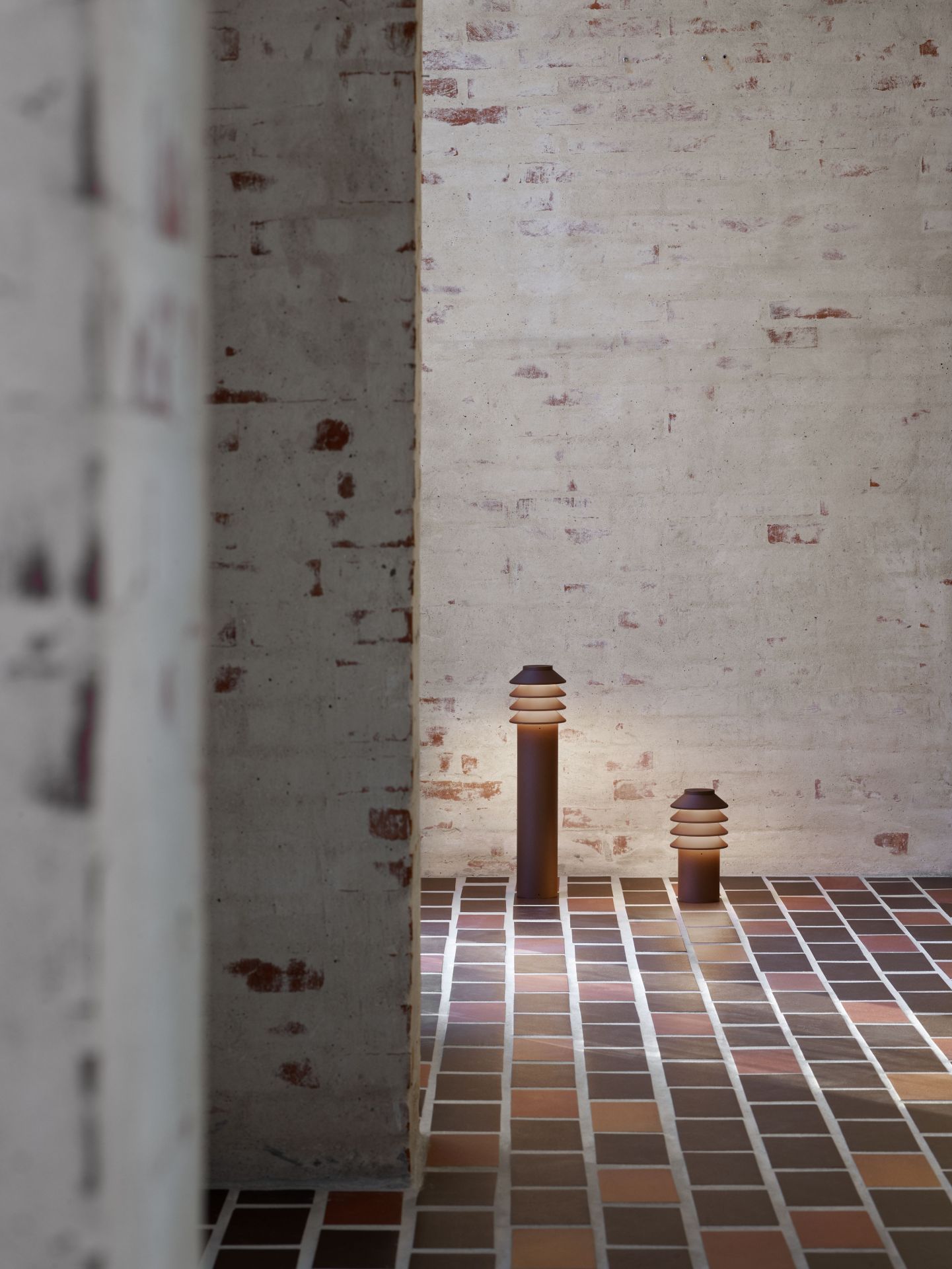 Zwei Bysted Garten Pollerleuchten von Louis Poulsen beleuchten einen gefliesten Außenbereich.