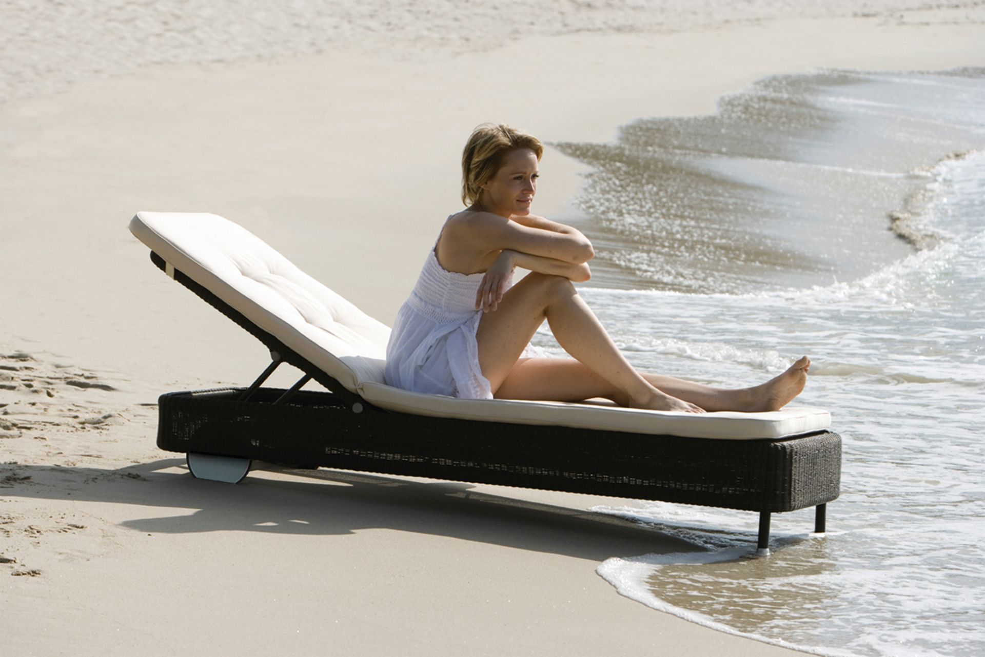 Frau entspannt auf Cane-Line Sonnenliege taupe am Strand. Outdoor Liege mit komfortabler Polsterung.