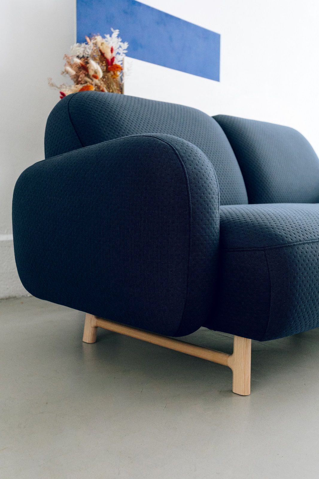 Nahaufnahme des blauen Hartô Auguste Sofas mit drei Sitzen und Holzbeinen.