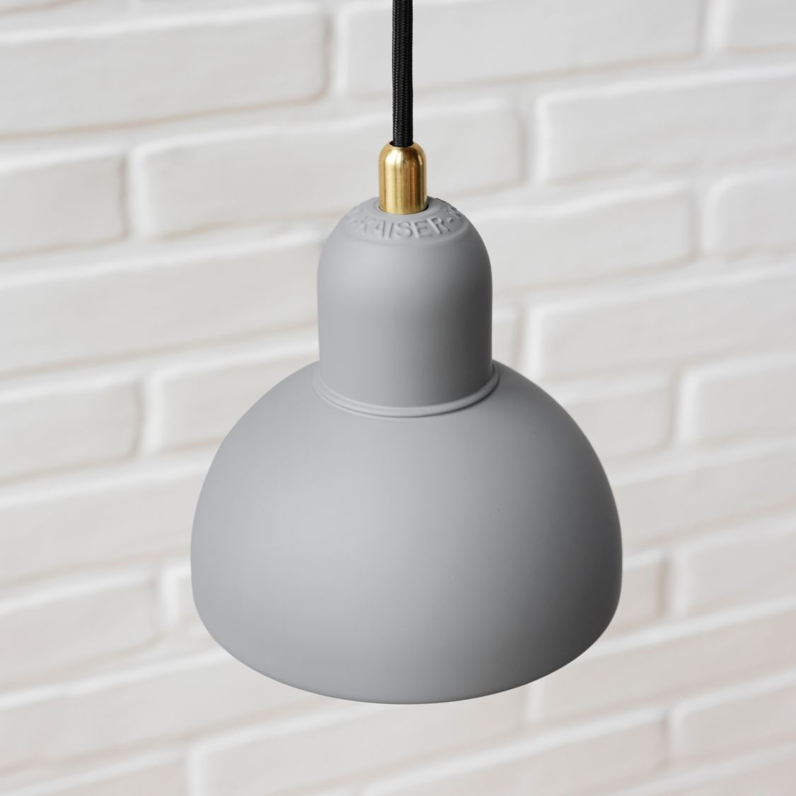 Graue 6722-P Pendelleuchte von Fritz Hansen mit schwarzem Kabel vor einer weißen Ziegelwand.